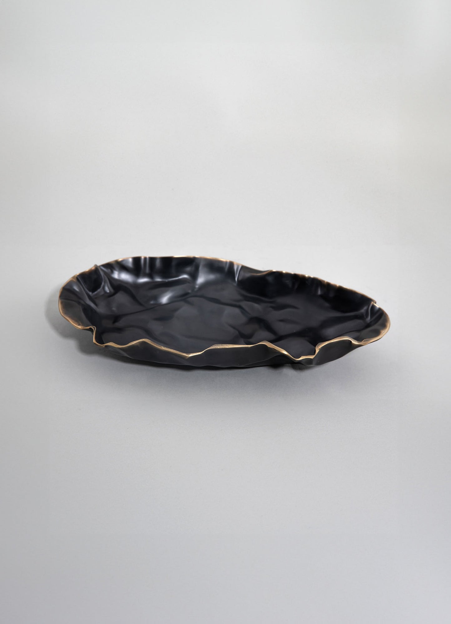 A black ceramic dish with an irregular, organic shape and a gold-colored rim, featuring a glossy finish.