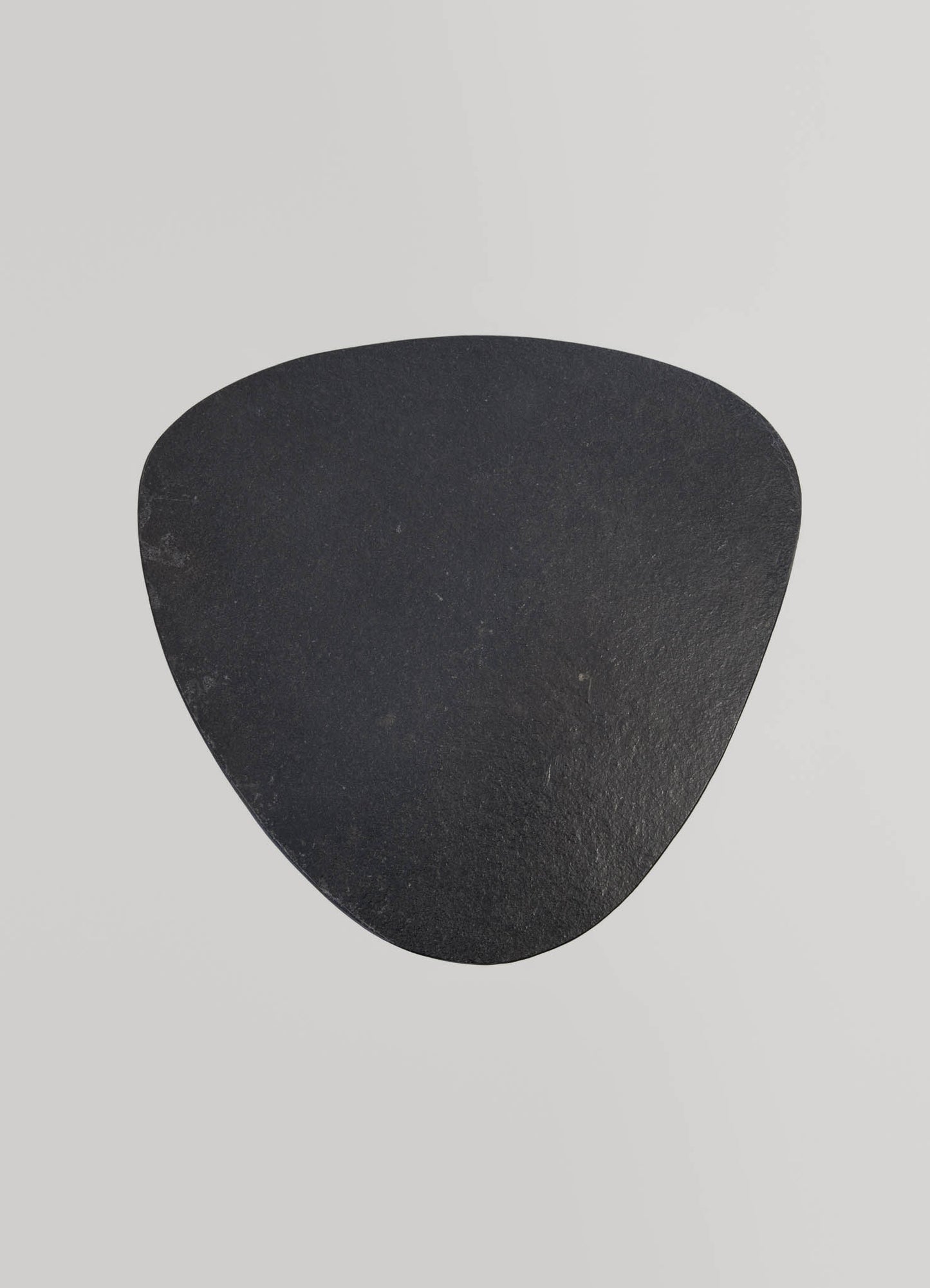 A black, triangular-shaped stone object with a textured surface, set against a light grey background.