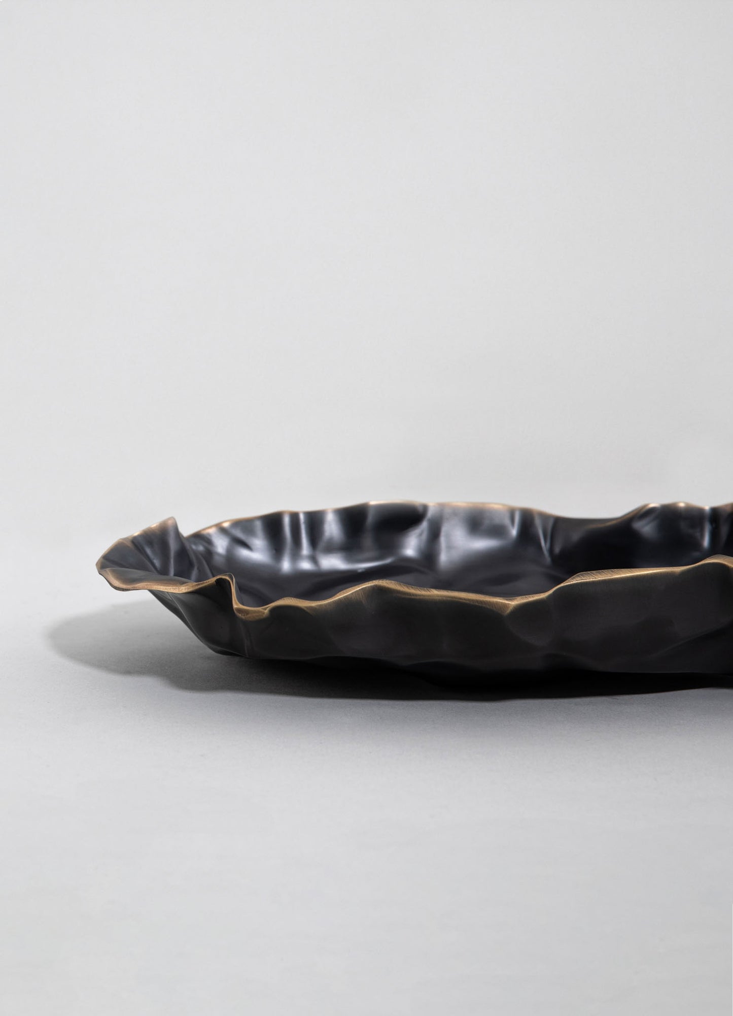 A decorative bowl with a wavy, irregular edge made of dark, glossy material resembling ceramic or glass, set against a plain, light-colored background.