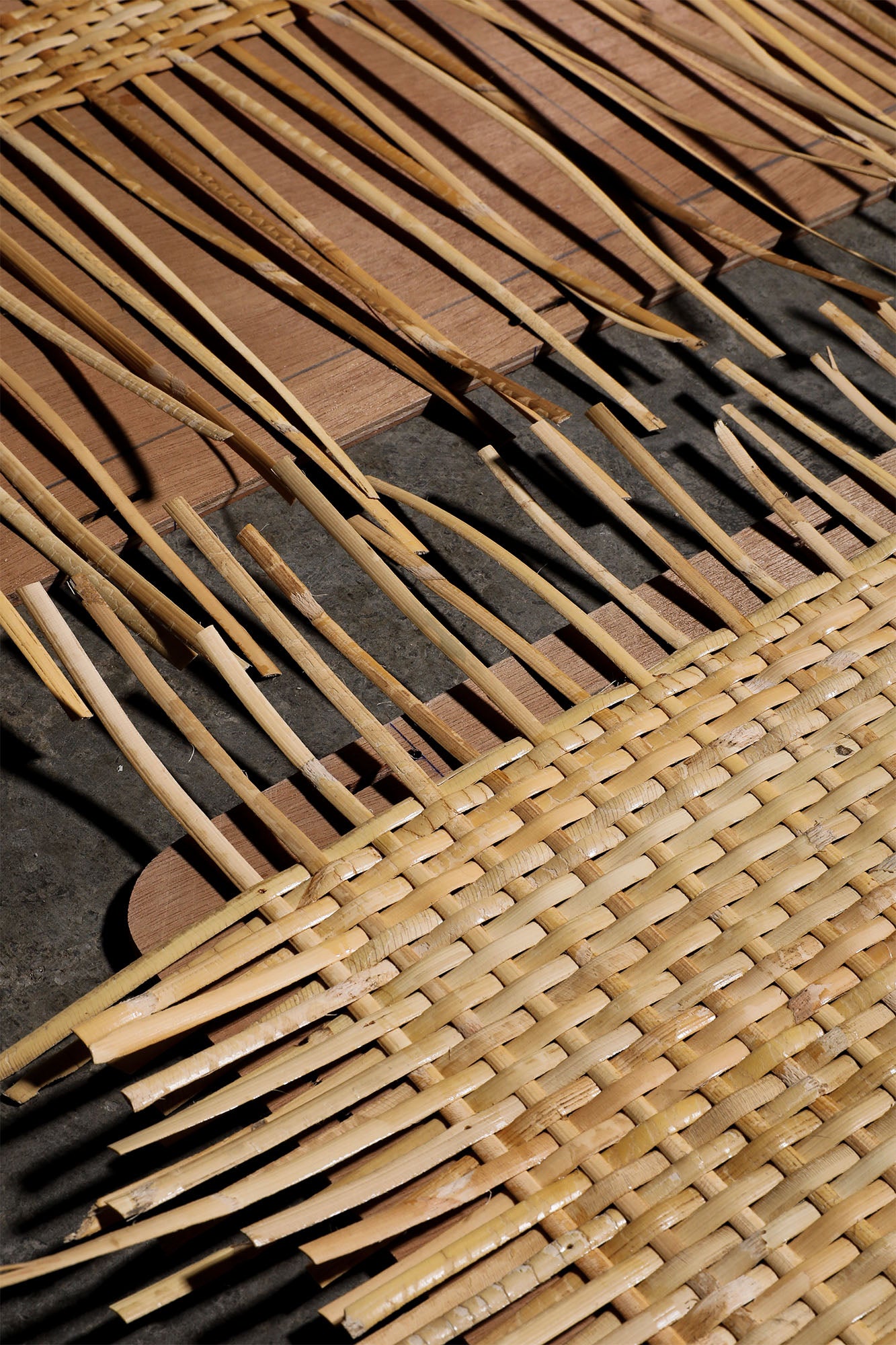 Woven rattan furniture with a natural, light beige tone featuring an intricate pattern of interlaced strips, complemented by vertical wooden slats. The design emphasizes handcrafted rustic style with organic materials and textures.