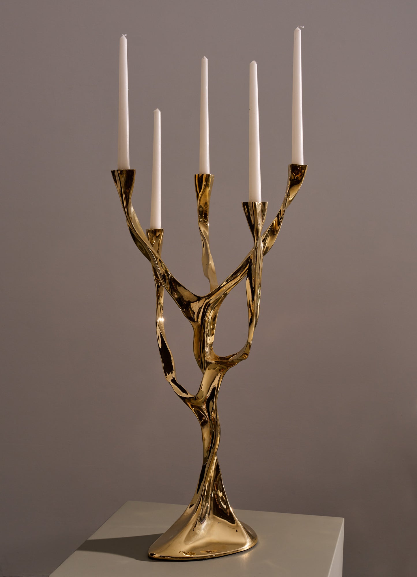 Brass candle holder with a sculptural, twisted organic design, holding five white taper candles, set against a neutral background.