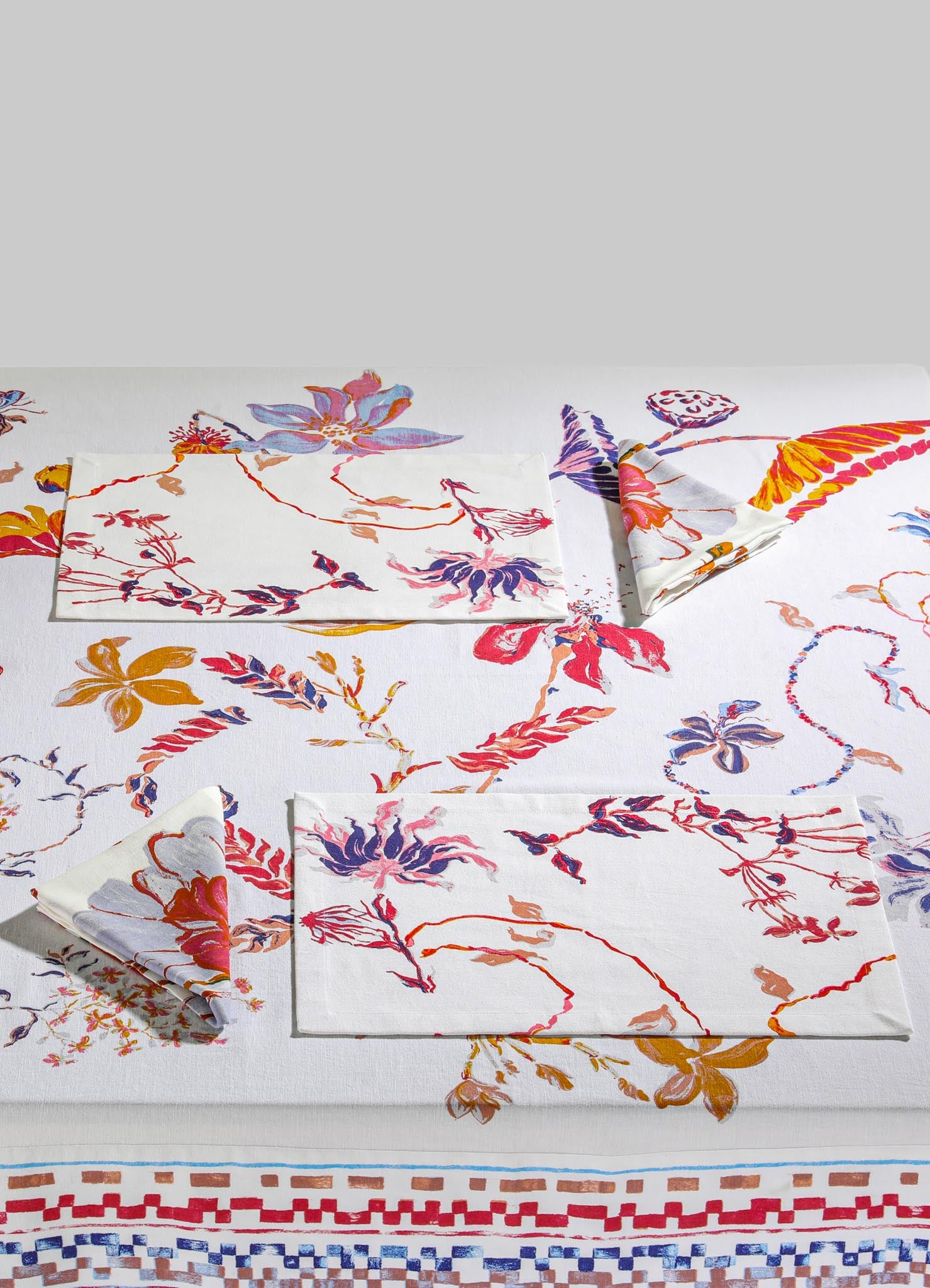 Decorative table linen set including a floral printed tablecloth, matching napkins, and a silk or cotton handkerchief in vibrant shades of red, purple, pink, and orange, with botanical and floral motifs.