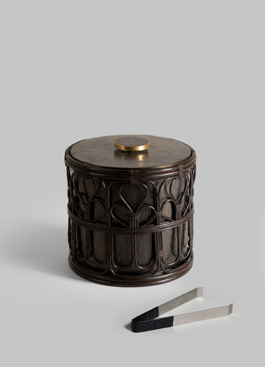 The VIYA Manipur Ice Bucket Large, featuring a carved dark wood finish and a hand-beaten brass knob, stands beside metal ice tongs on a light gray background—a sophisticated upgrade to your barware collection.
