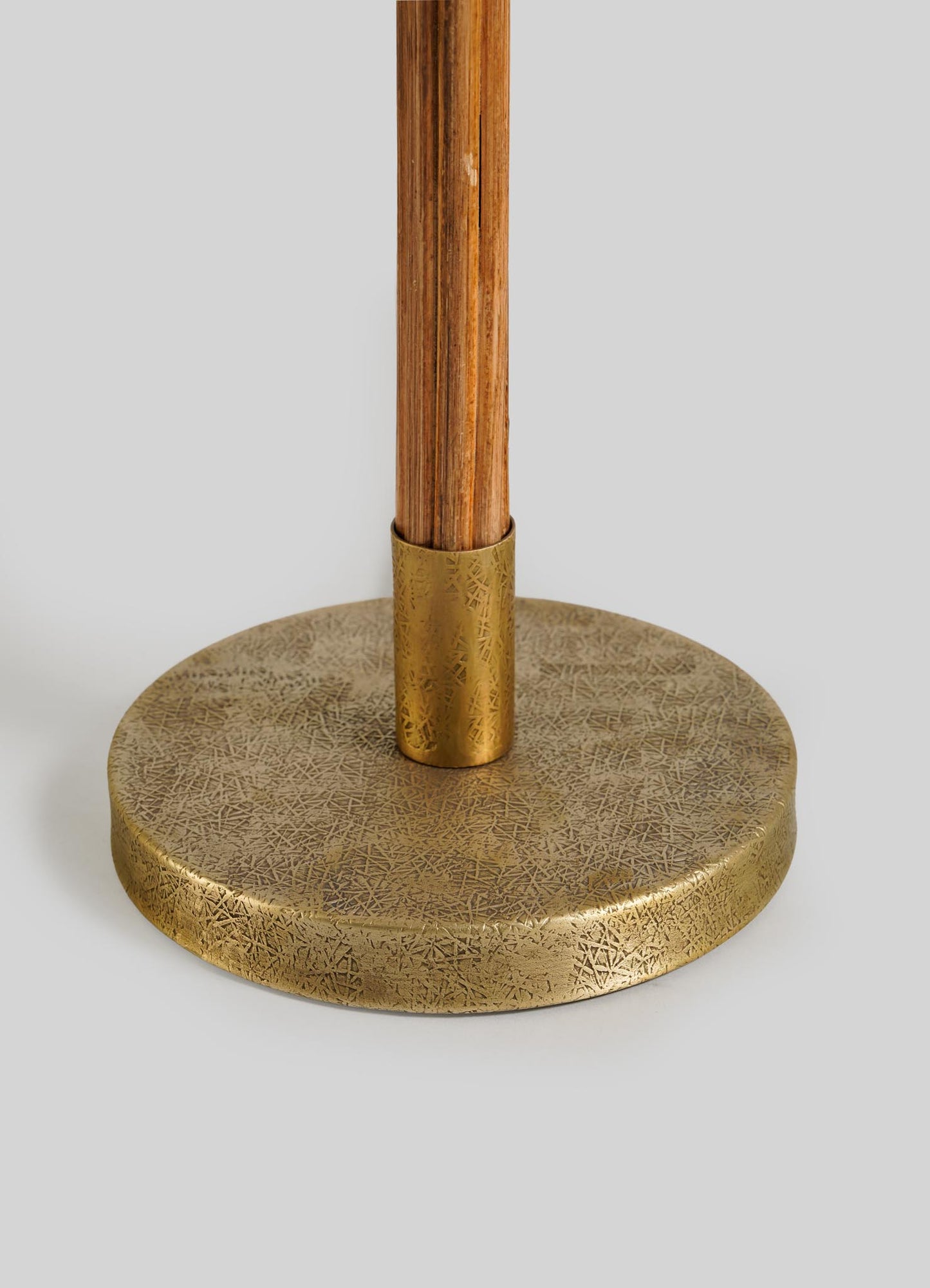 Close-up of the Namsai Floor Lamp Round by VIYA, showing its textured brass circular base with a central wooden pole and elegant brass trimmings. A light gray background enhances the metallic and natural wood accents.