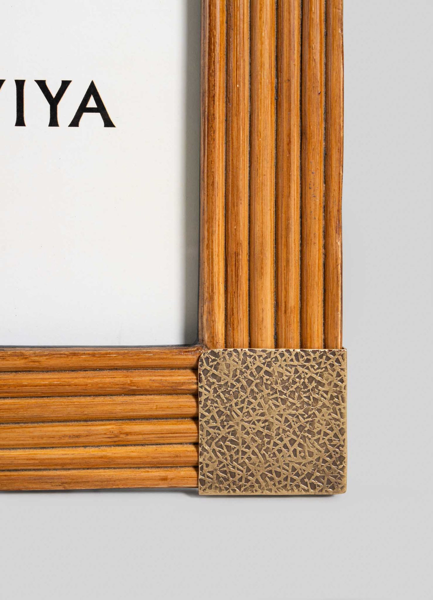 Close-up of the corner of a VIYA Namsai Photo Frame Small, featuring vertical grooves, brass corner trimmings, and partial black text on a white background inside the frame.