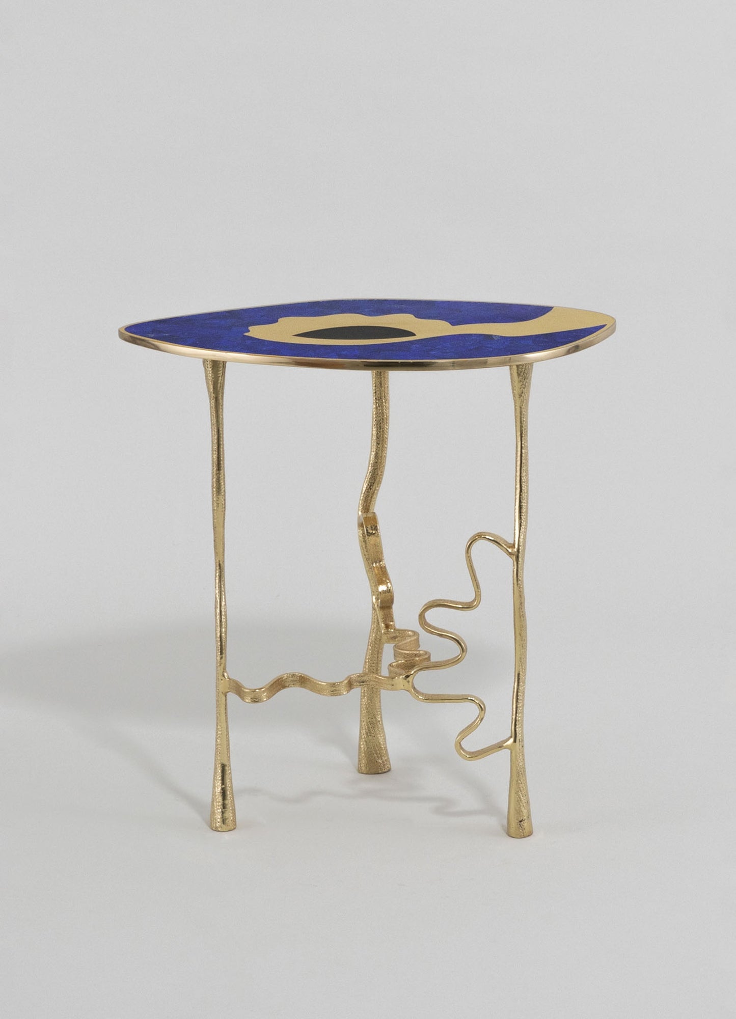A small accent table with a round top in deep blue with gold abstract motifs, supported by sculptural gold metal legs with organic, freeform shapes.