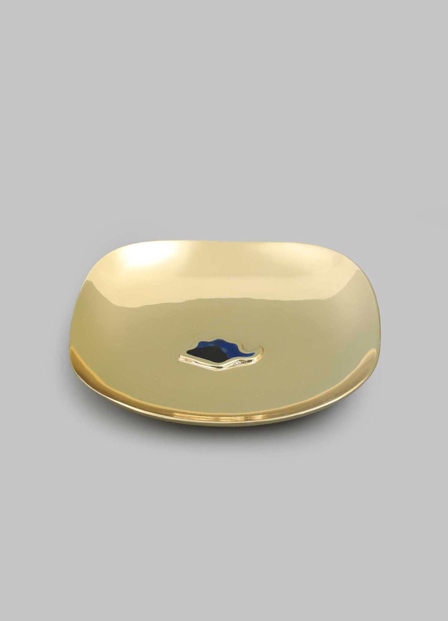 The VIYA Nazar Battu Trinket Bowl Large features a shiny gold-tone, square shape with rounded edges, set against a gray background. Its center displays an abstract blue and black motif inspired by the modern Nazar amulet.