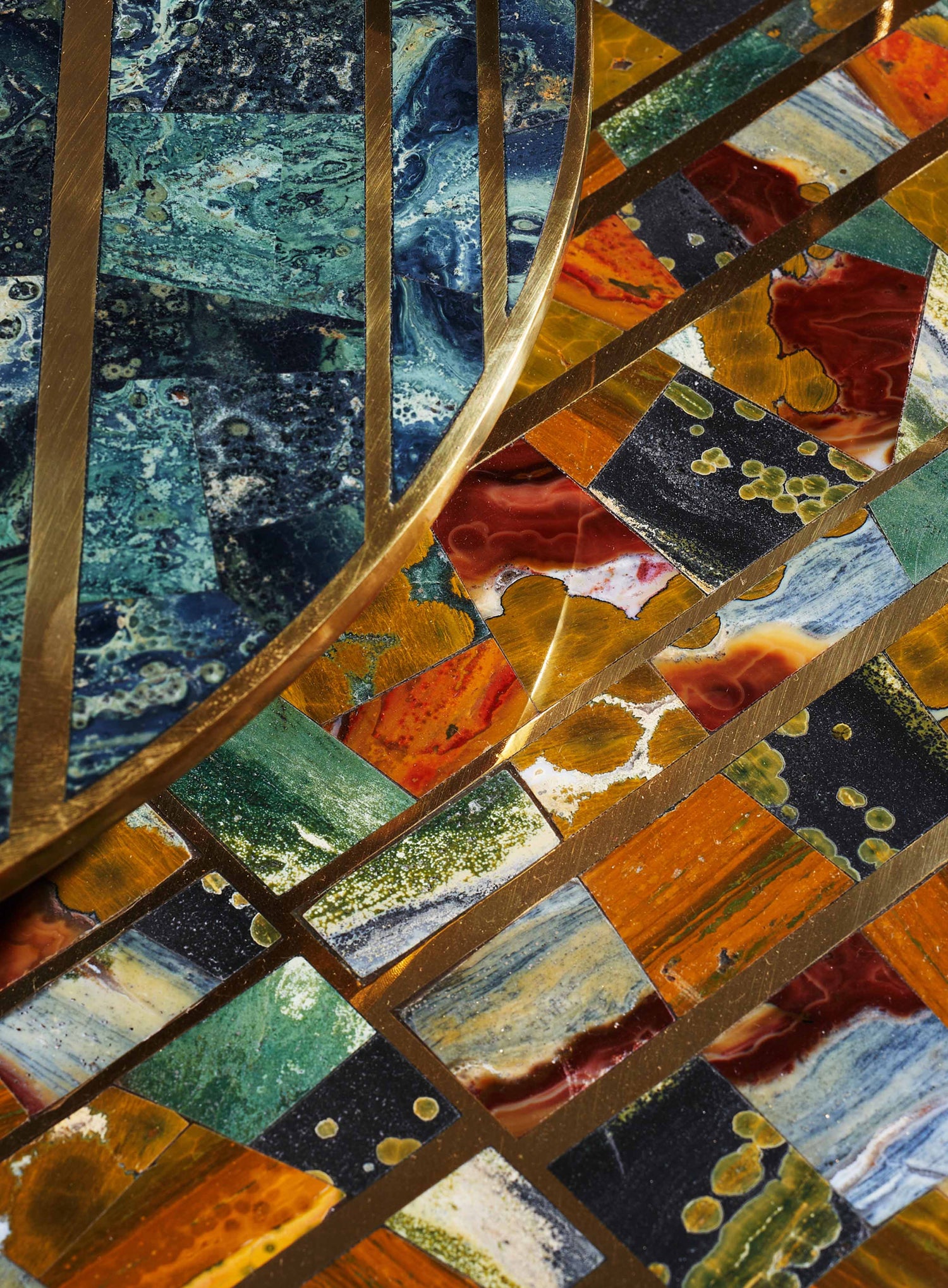 Colorful mosaic tabletop with irregular stone tiles in shades of blue, red, green, black, and orange, accented by gold metal strips creating geometric patterns, giving a vibrant and contemporary design.