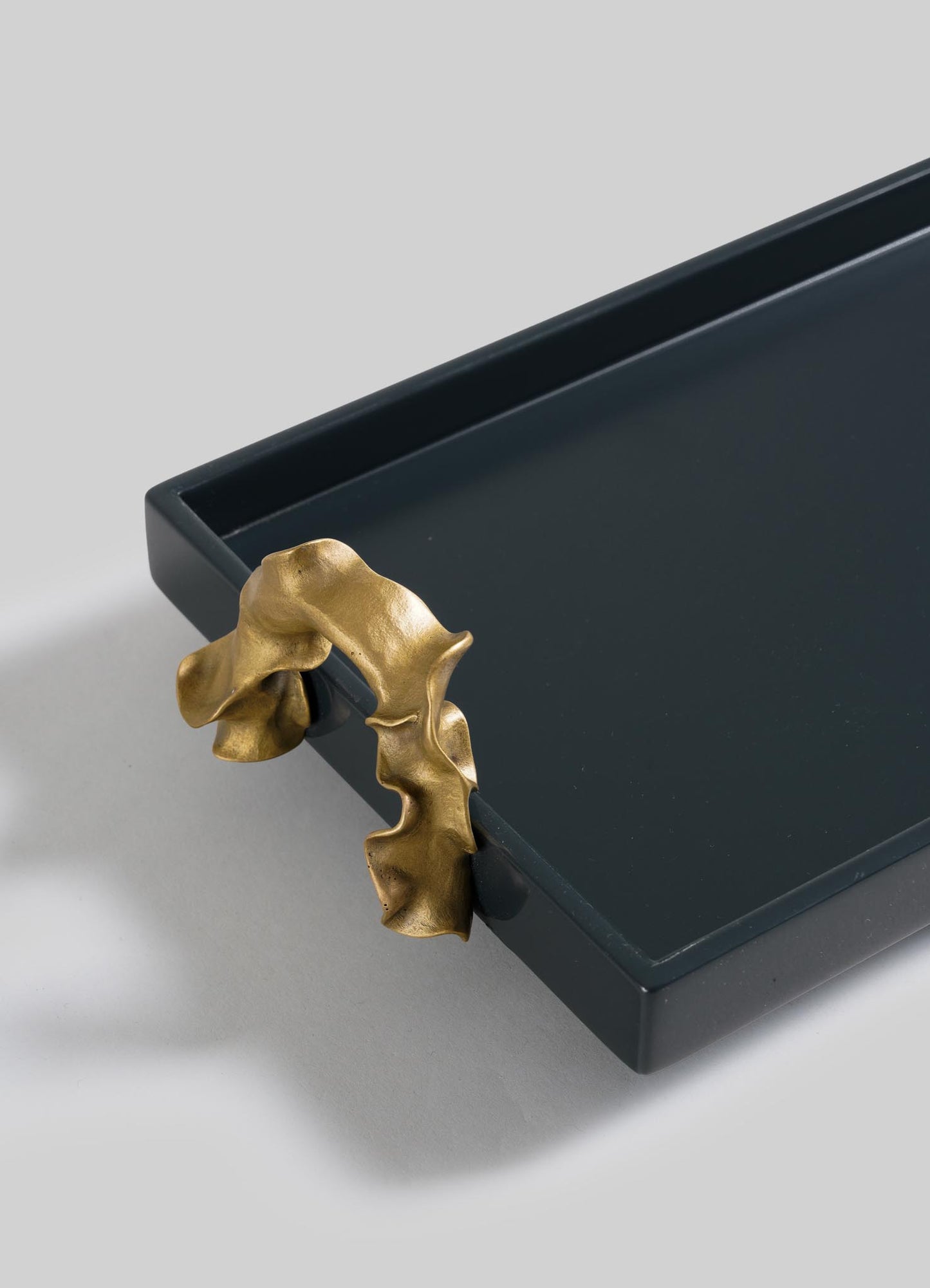 The VIYA Saffron Dark Blue Vanity Tray is a dark rectangular tray with raised edges, accented by a sculptural gold handle inspired by folded saffron threads and elegantly attached to one corner.