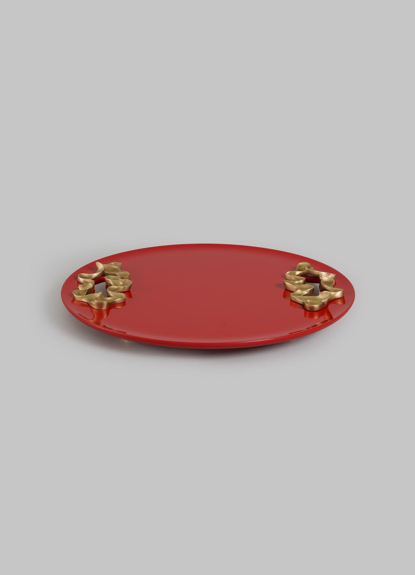 The Saffron Red Tray Small by VIYA features a round, flat design in rich red with smooth edges and two clusters of gold abstract floral accents, inspired by saffron threads, displayed against a plain light gray background.