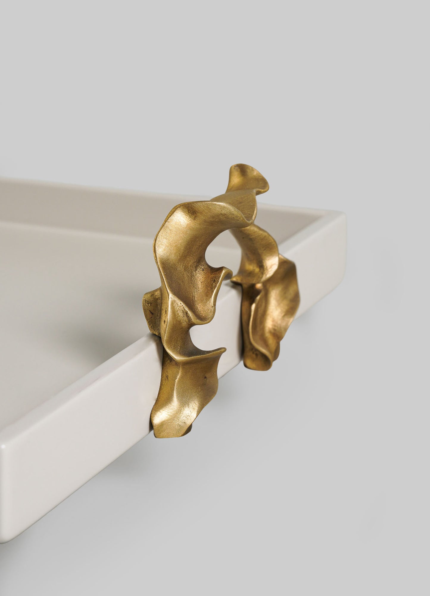 The Saffron Ecru Towel Tray by VIYA features sculptural, gold metal detailing that evokes delicate saffron threads draped over a smooth white surface, set against a minimalist grey background.