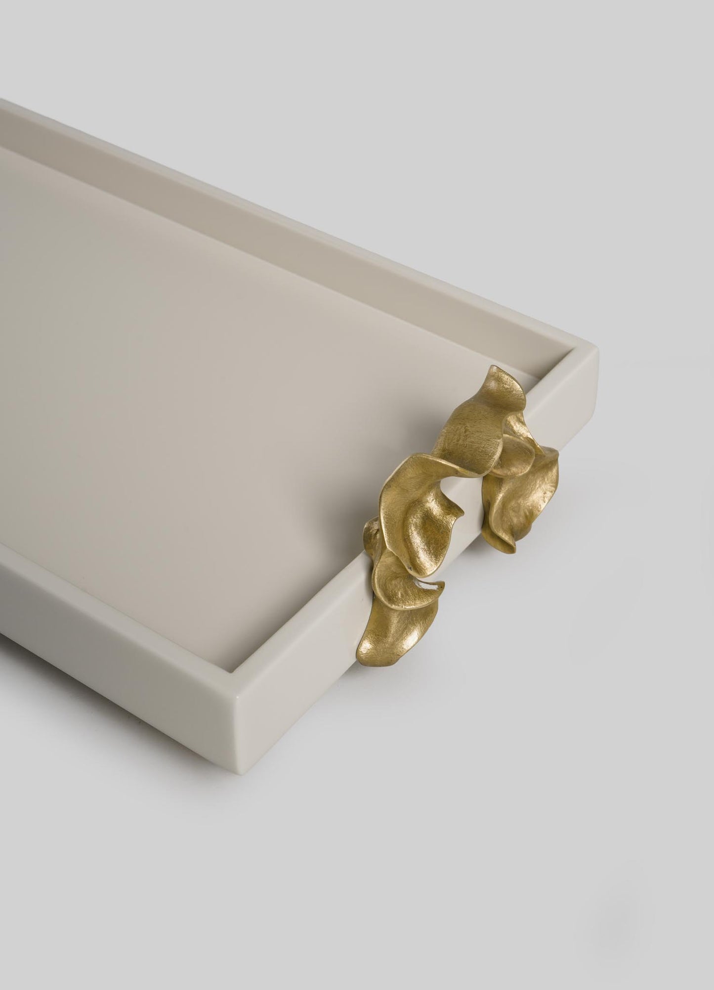 The VIYA Saffron Ecru Vanity Tray is a rectangular, off-white tray featuring a sculpted gold accent that resembles flowing leaves or draped fabric on one corner, set against a plain light gray background.