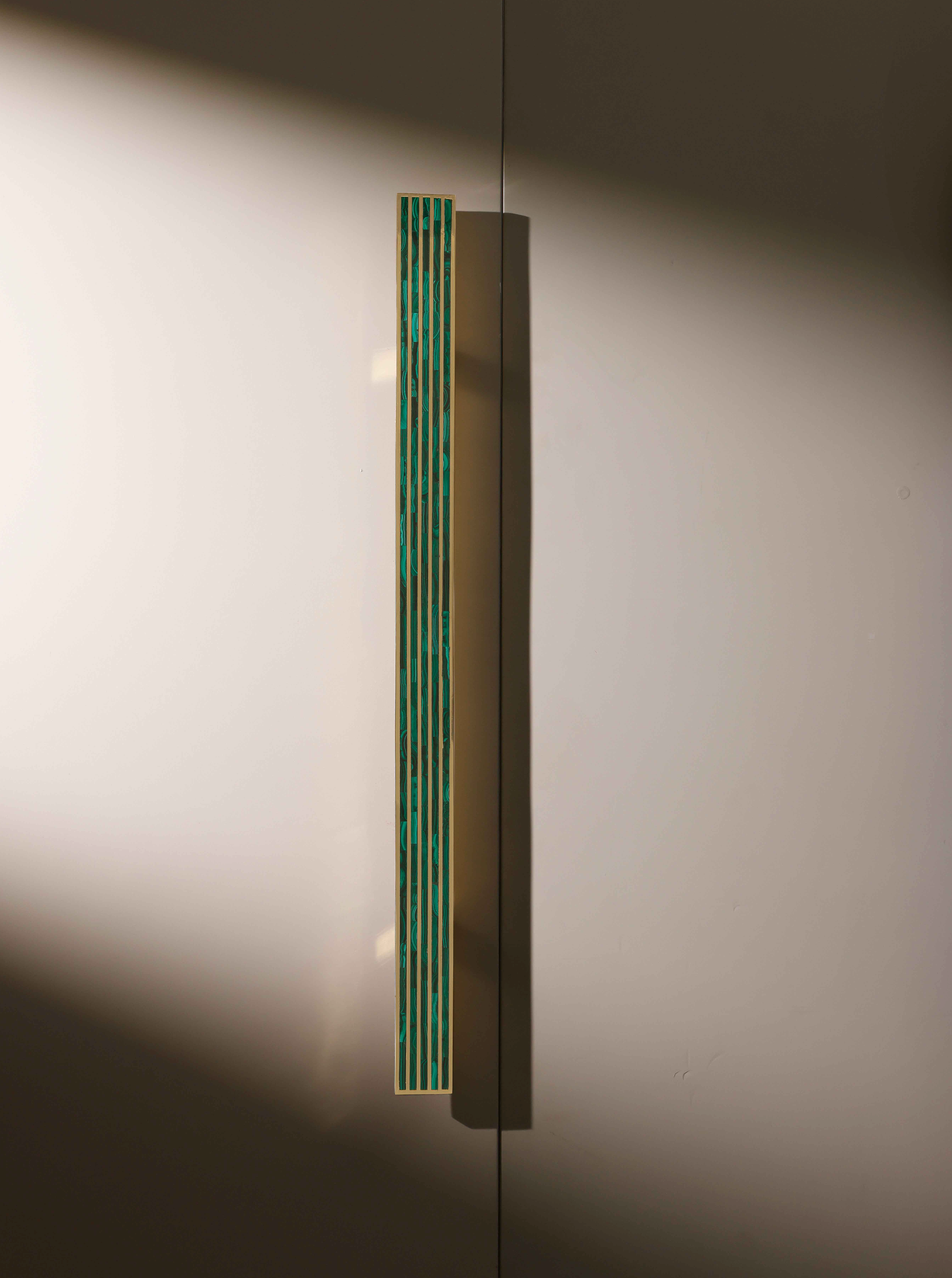 A close-up of a modern cabinet or door handle with a slim, vertical design featuring geometric cutouts and a teal color accents, mounted on a smooth, beige surface.