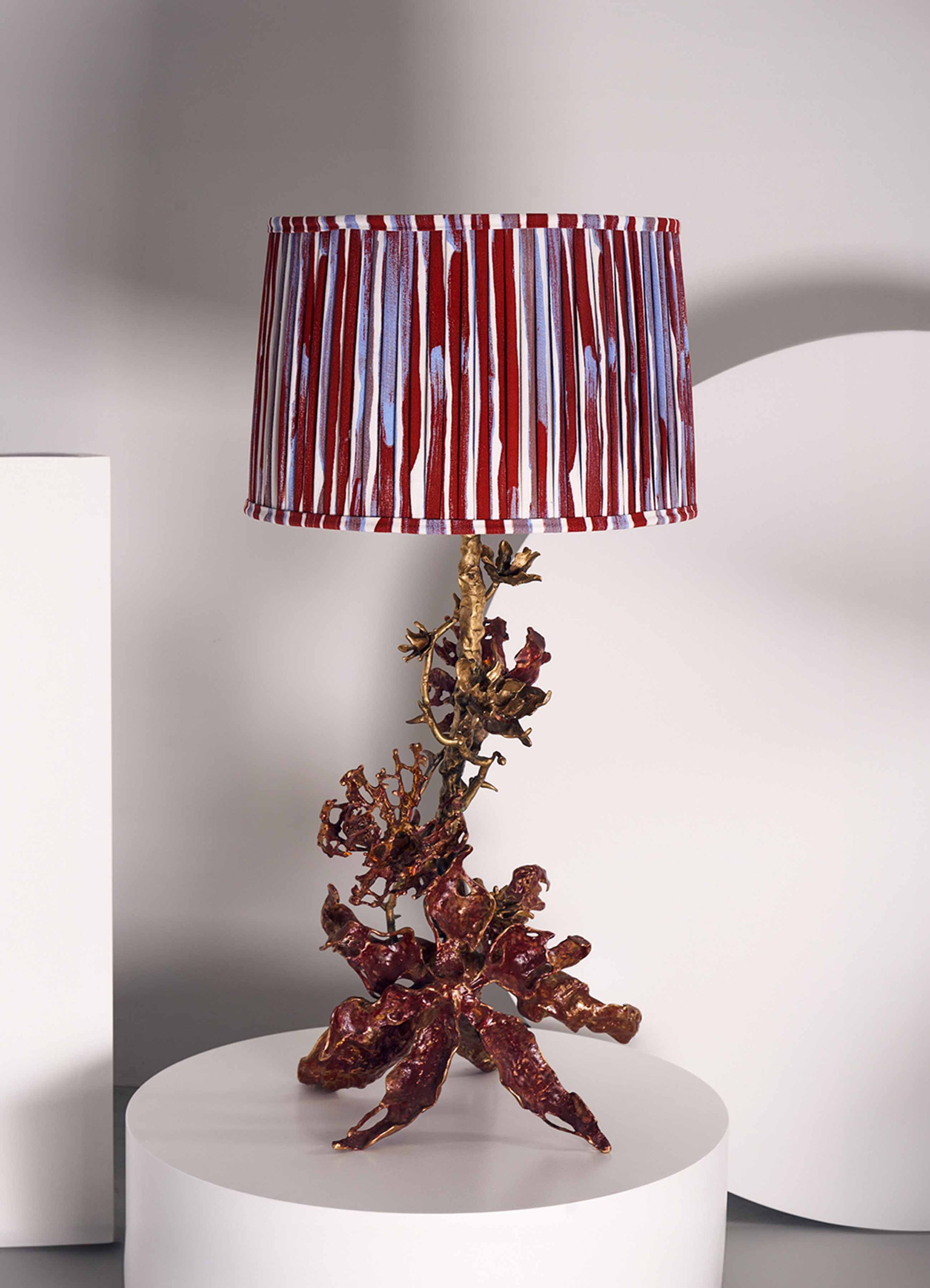 Decorative table lamp with a sculptural base resembling coral or organic branches, finished in metallic bronze and red hues, topped with a fabric lampshade featuring bold red, white, and purple vertical stripes.