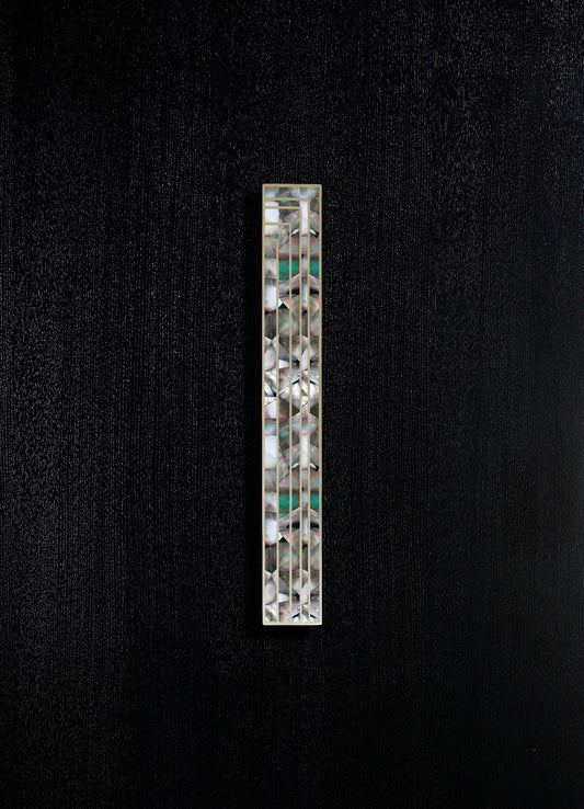 A tall, narrow decorative object featuring an iridescent, shell-like motif with geometric patterns, framed in metal, set against a textured black background.