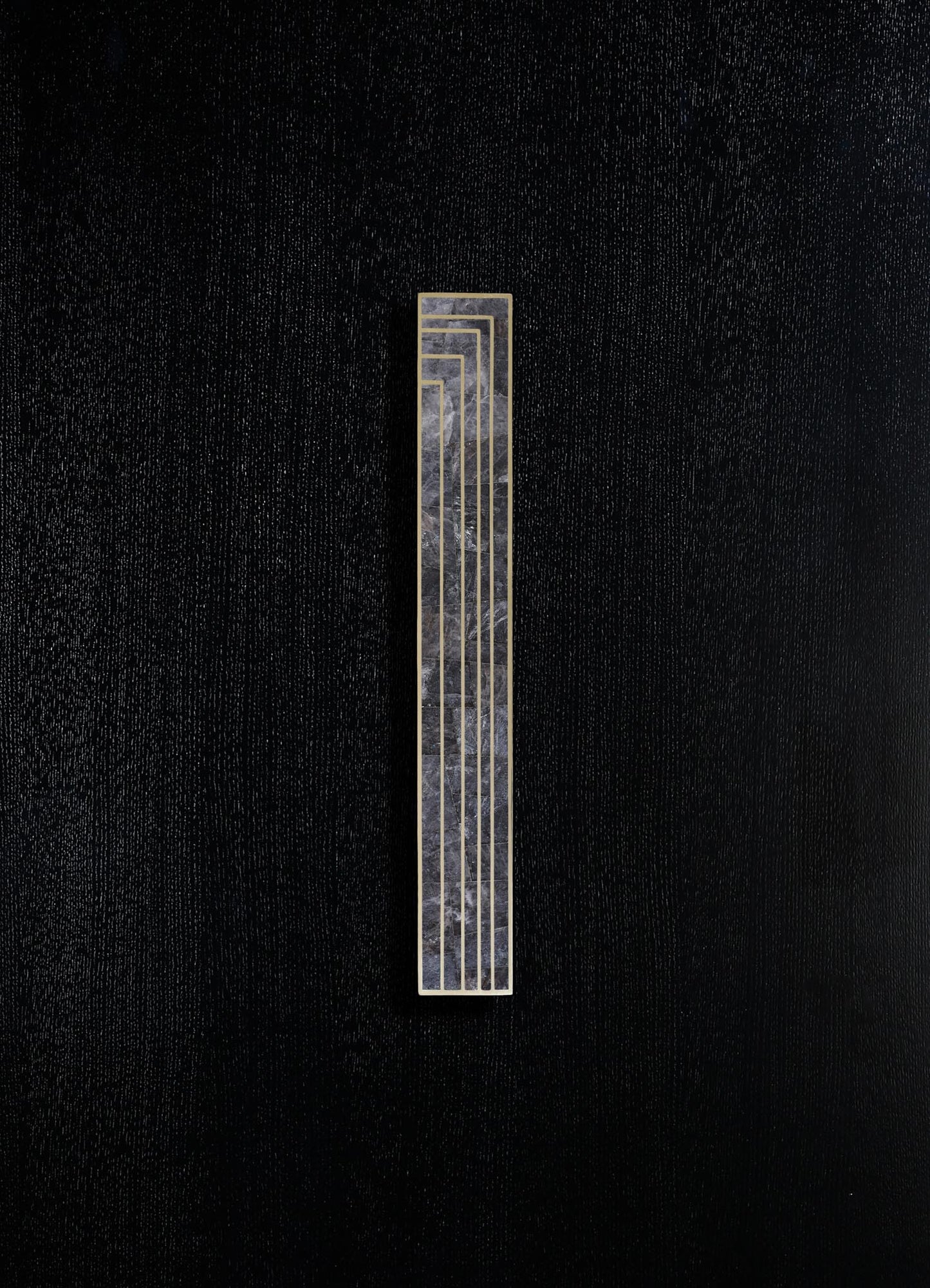 A decorative wall panel featuring a narrow vertical design with a black and gray marbled surface encased in a gold frame, mounted on a textured black wall.