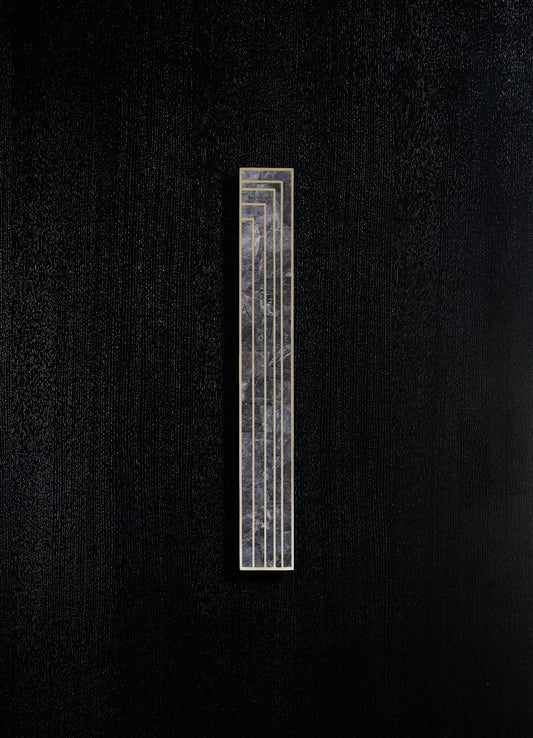 A decorative wall panel featuring a narrow vertical design with a black and gray marbled surface encased in a gold frame, mounted on a textured black wall.