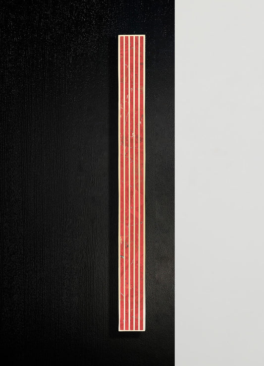A vertical mosaic tile with red and beige geometric patterns, mounted on a black background with a neutral-colored wall on the right side.