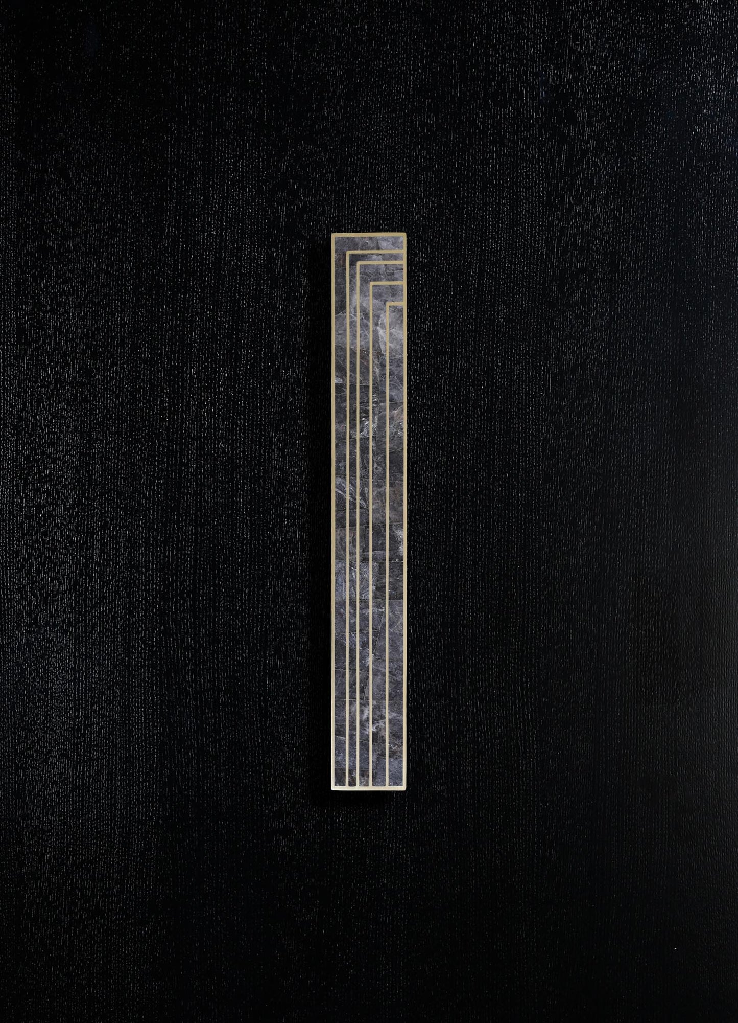 A rectangular black marble wall sconce with gold geometric lines, mounted on a textured black surface.