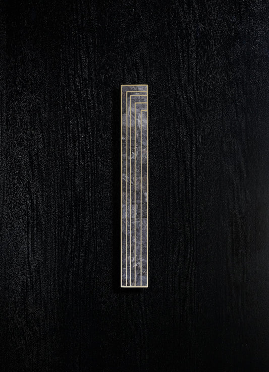 A rectangular black marble wall sconce with gold geometric lines, mounted on a textured black surface.