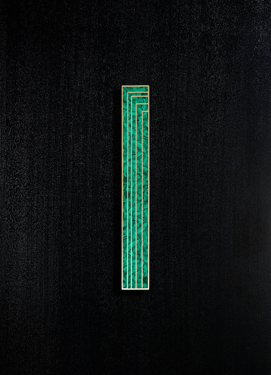A decorative object featuring a rectangular panel with a geometric pattern in shades of green and gold accents, set against a black textured background.