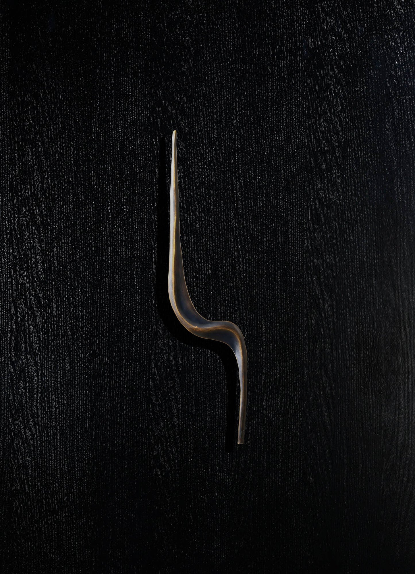 A sleek, modern candle snuffer with a curved, elongated metal handle in black and gold tones, set against a textured dark background.