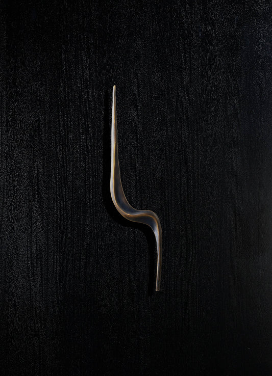 A sleek, modern candle snuffer with a curved, elongated metal handle in black and gold tones, set against a textured dark background.