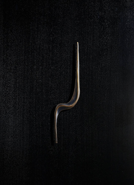 A ceramic wall sculpture featuring an abstract, elongated shape with a smooth, glossy finish in neutral tones against a black textured background.