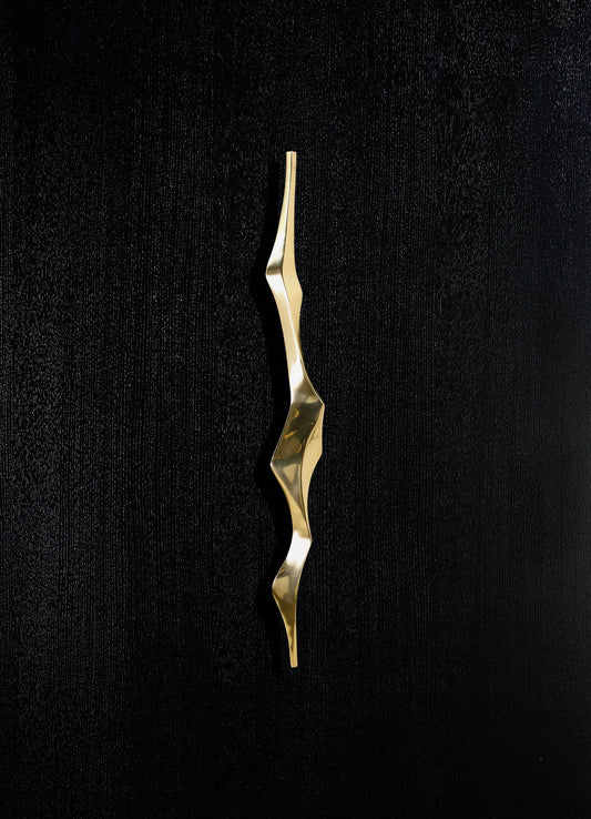 A gold-toned metal sculpture with an abstract, wavy form, mounted on a black textured surface.
