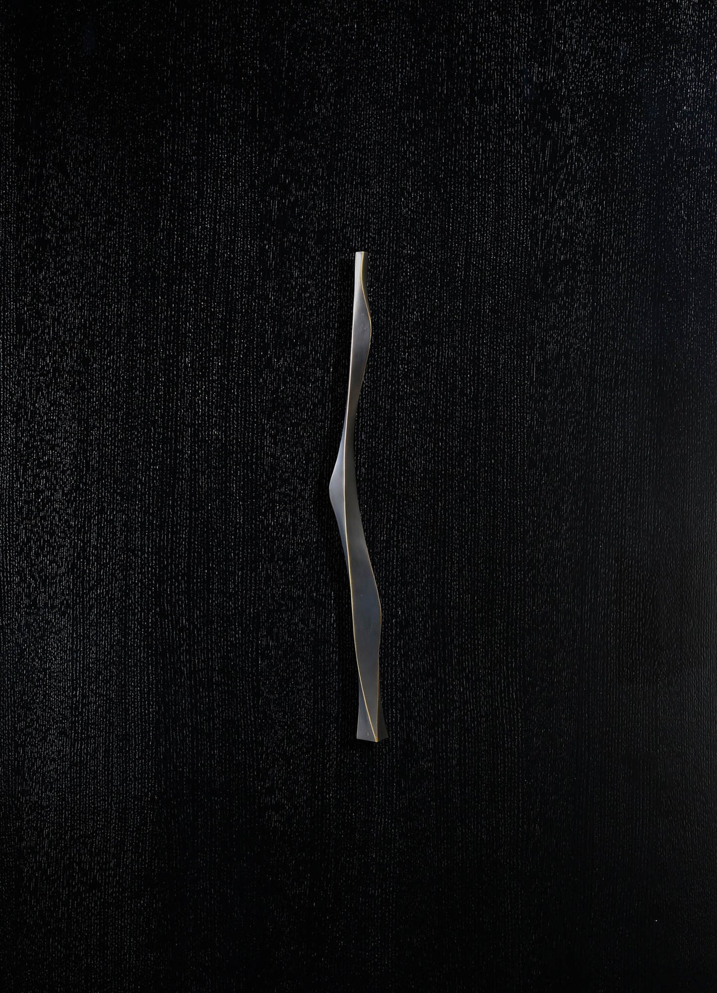 A sleek, metallic sculpture with a wavy, twisting form, finished in matte silver. The sculpture is set against a textured black background, emphasizing its modern, contemporary style.