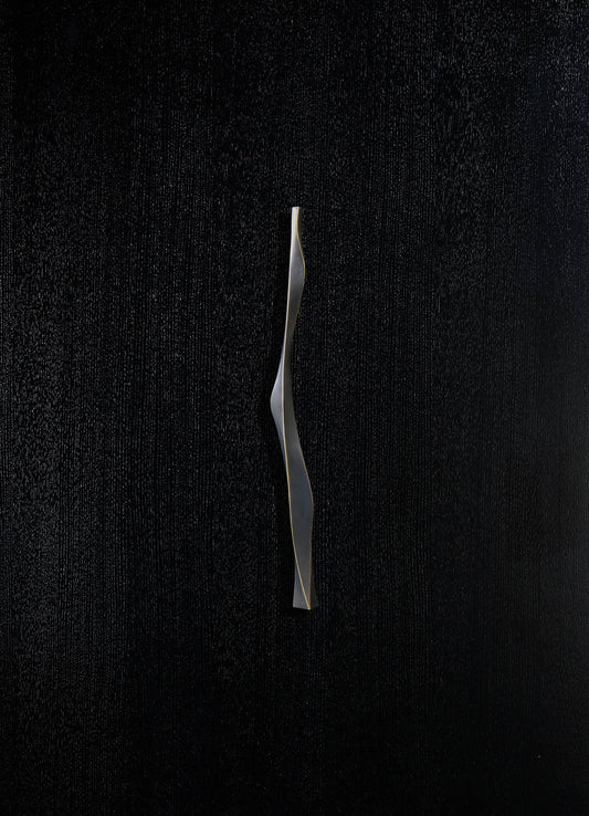 A sleek, metallic sculpture with a wavy, twisting form, finished in matte silver. The sculpture is set against a textured black background, emphasizing its modern, contemporary style.