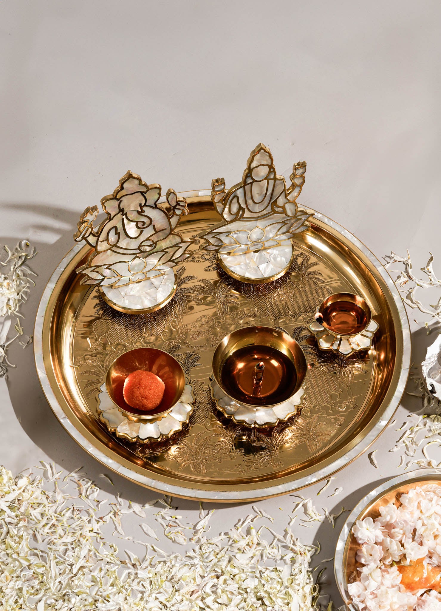A decorative brass tray with an engraved landscape design holds two mother-of-pearl lotus flower candle holders, one with a small bronze bowl and another with a rounded object, all showcasing a luxurious and intricate craftsmanship style.