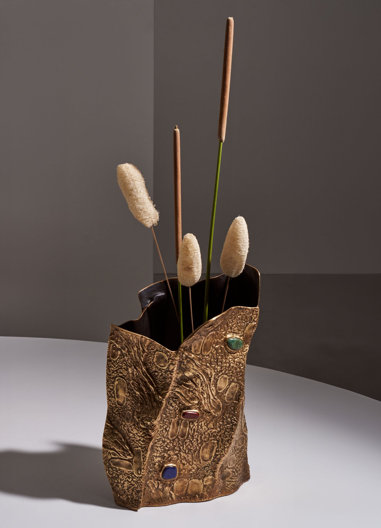 Decorative ceramic vase with textured, gold-toned surface and colorful embedded stones, holding dried reeds and grasses in neutral beige and brown tones.