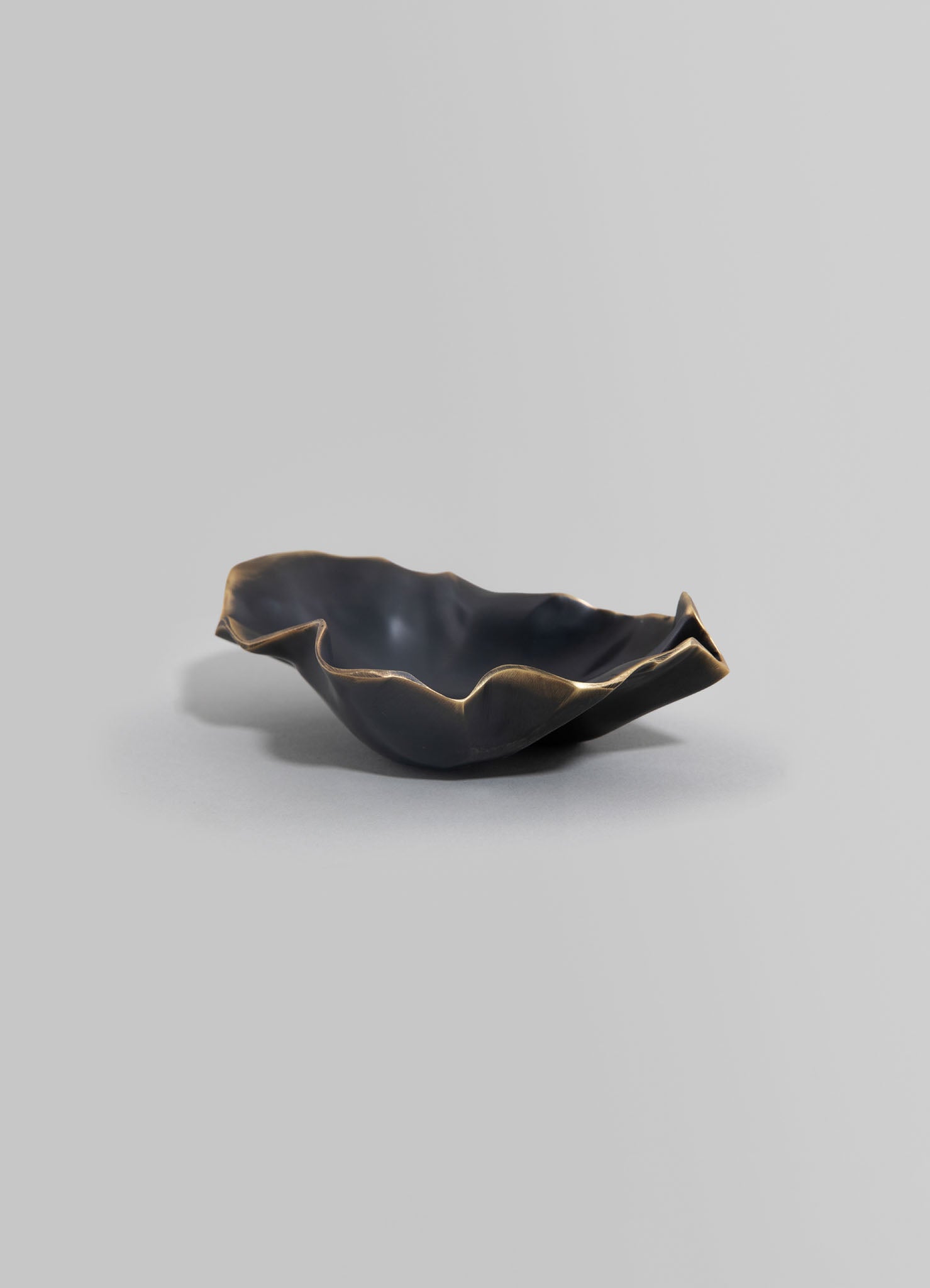 A black ceramic bowl with irregular, wavy edges and a glossy finish, placed on a neutral gray background.