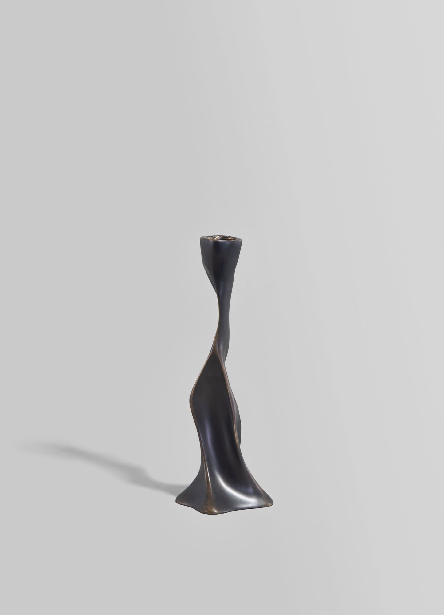A sculptural candle holder made of black metal with a twisted, organic form and a matte finish, set against a neutral gray background.
