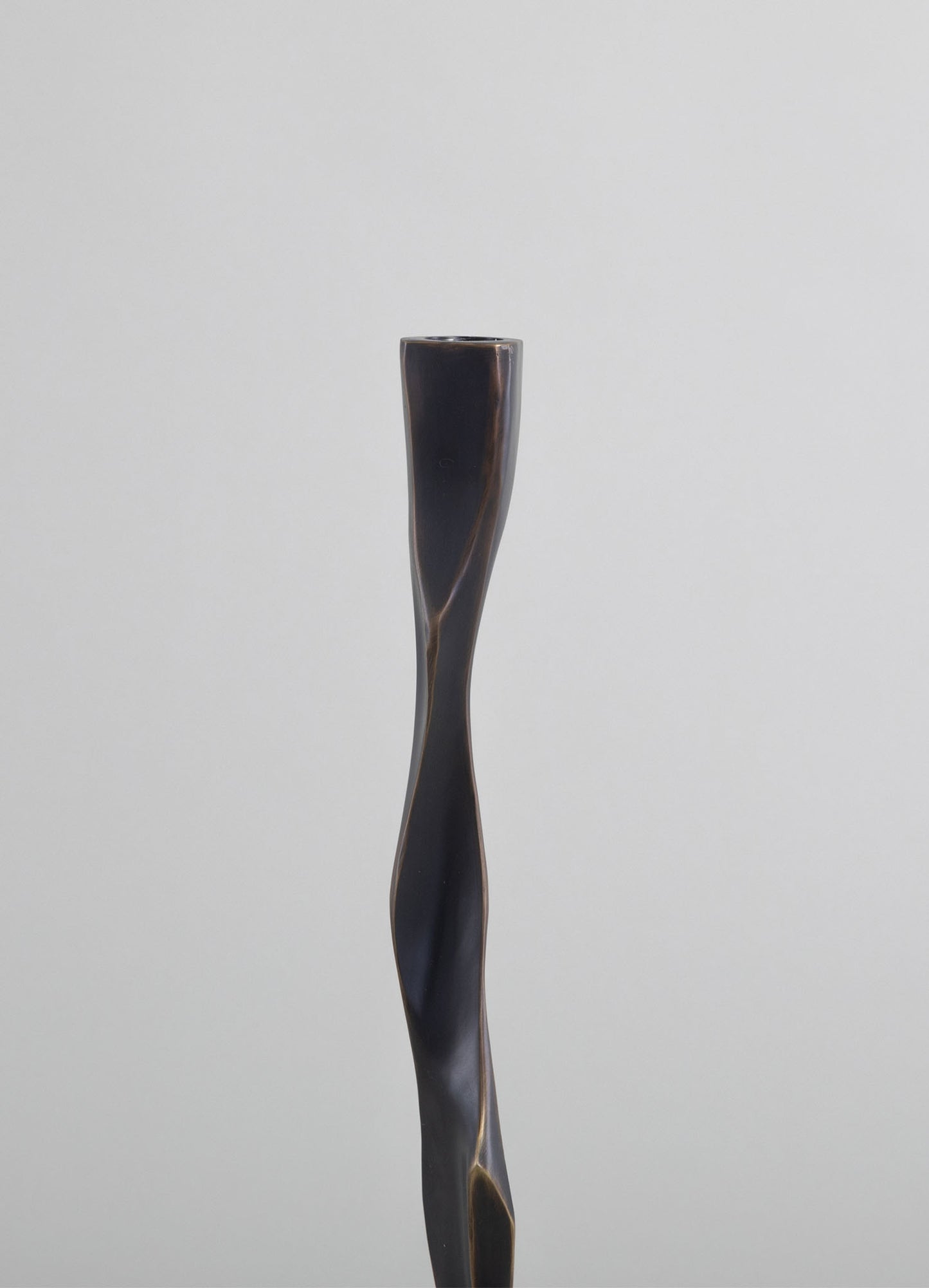 A tall, curvaceous candle holder made of dark, polished wood with a smooth, twisted design. The finish has subtle tonal variations, emphasizing its handcrafted, contemporary style.