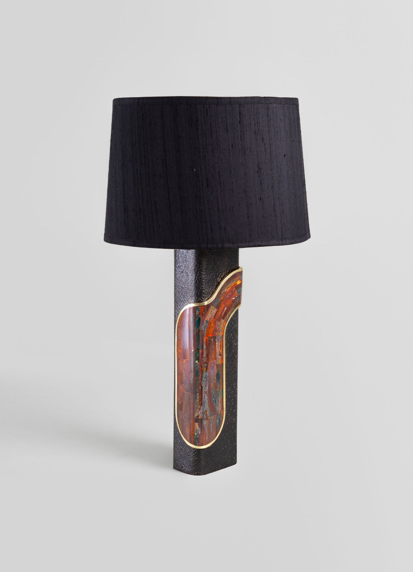 Table lamp with a textured black base featuring a colorful stone inset and gold trim, topped with a black fabric lampshade, in a contemporary style.