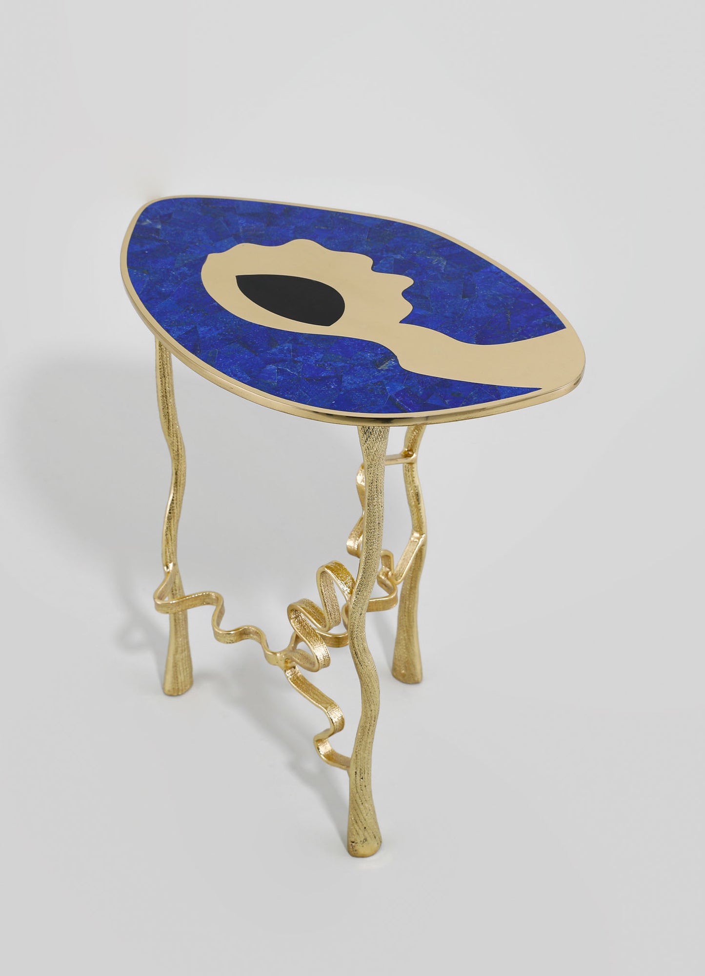A decorative side table with a top featuring a blue and black abstract motif set in a beige background, supported by gold-toned, irregularly shaped metal legs with a textured finish.