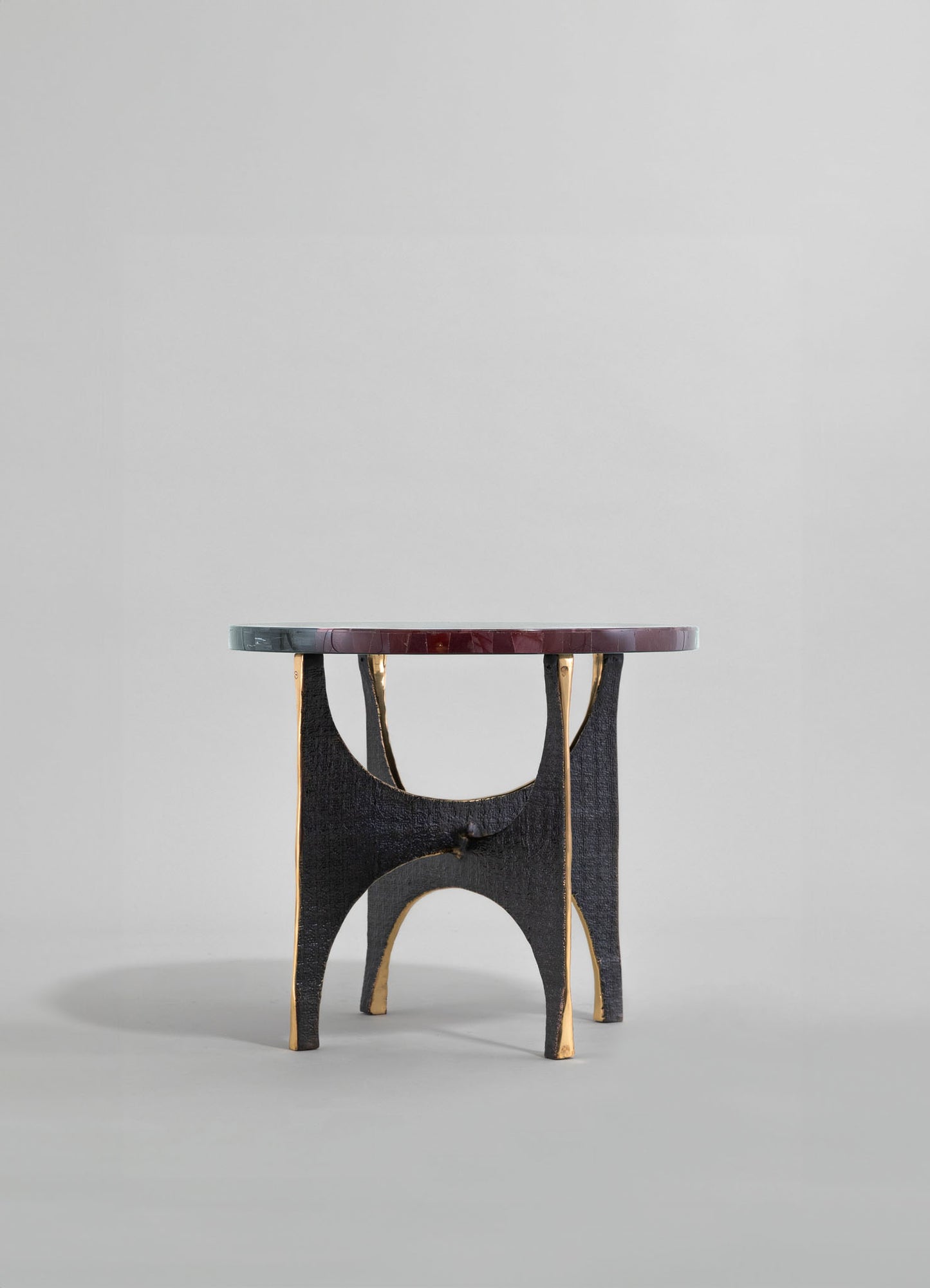 A small side table with a round marble top featuring shades of gray and burgundy, supported by a black wooden base with curved legs accented with gold trim, in a contemporary style.