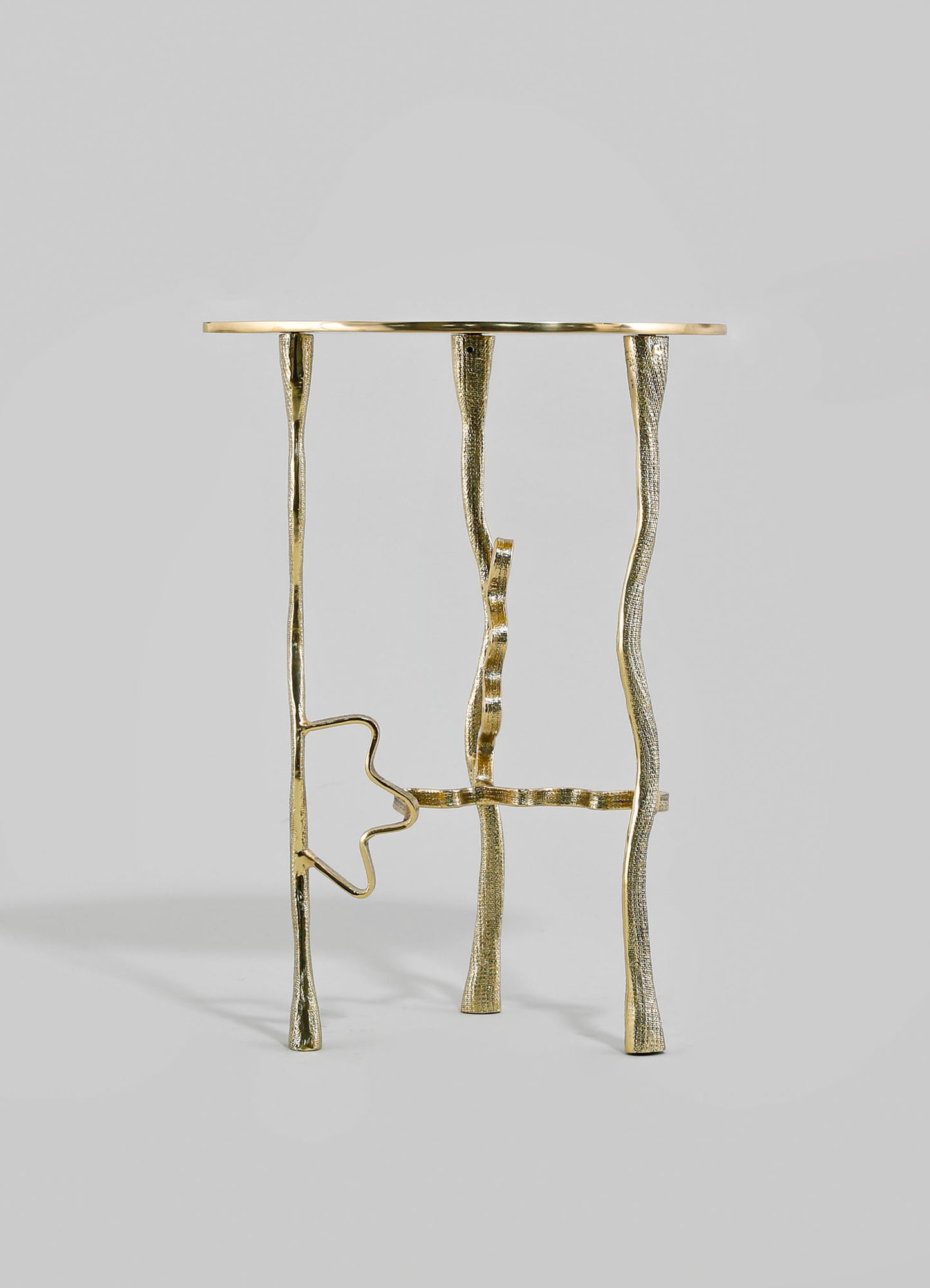 A brass side table with sculptural, irregularly shaped legs and a round top, featuring a textured, metallic finish in gold tones. The design has an modern, artistic style with organic motifs.