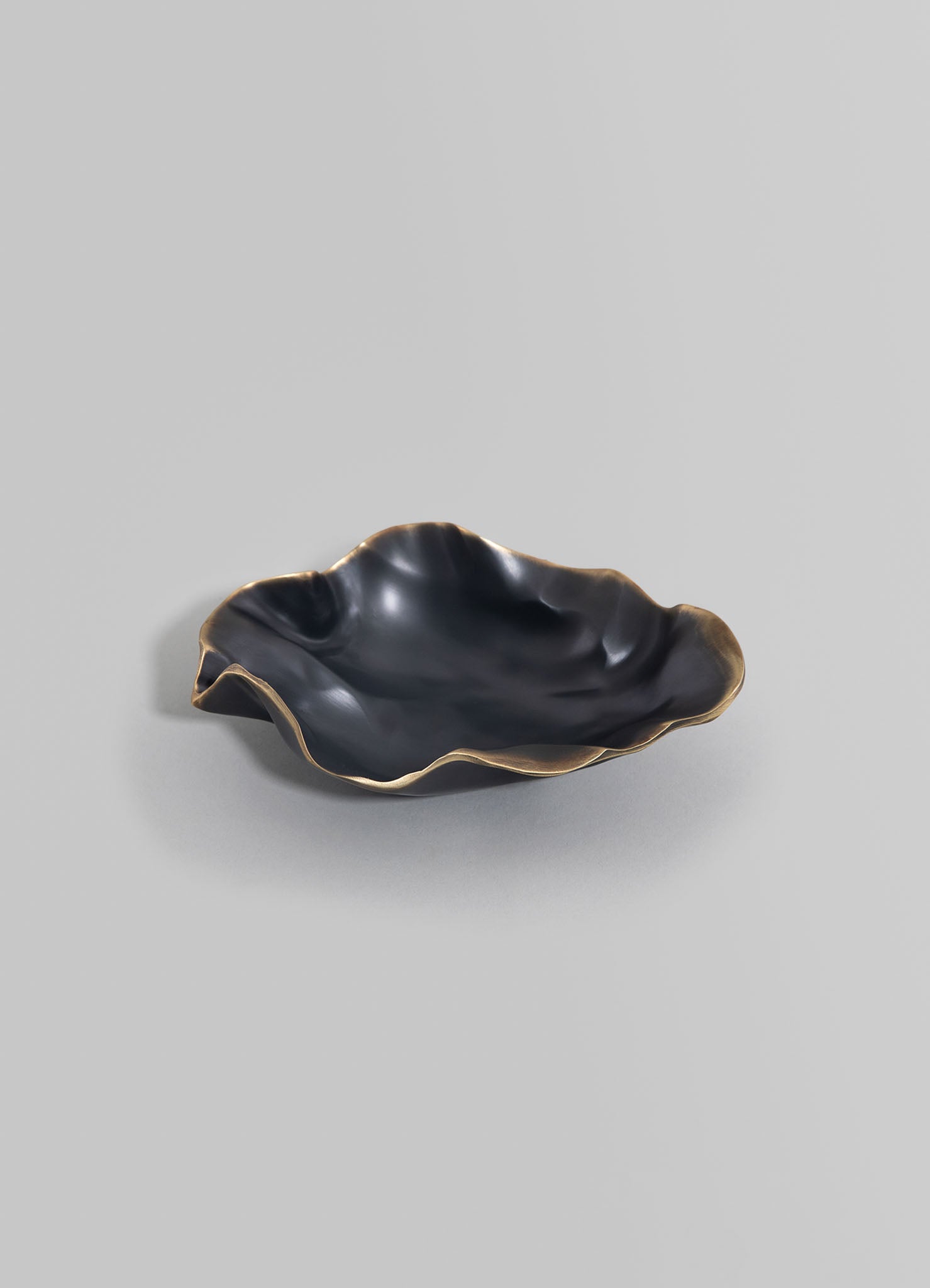 Black ceramic bowl with wavy, irregular edges and a matte finish, featuring bronze-colored accents along the rim, set against a plain light background.