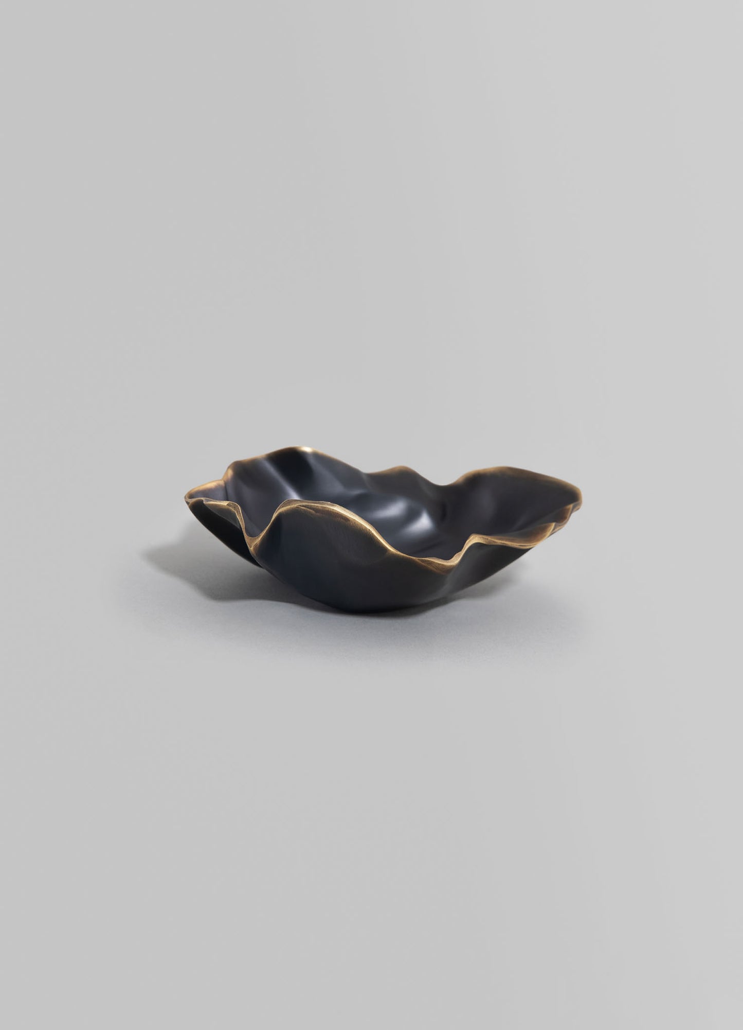 A black ceramic bowl with a gold-edged, irregular, and organic shape, featuring a textured, wavy rim on a neutral gray background.
