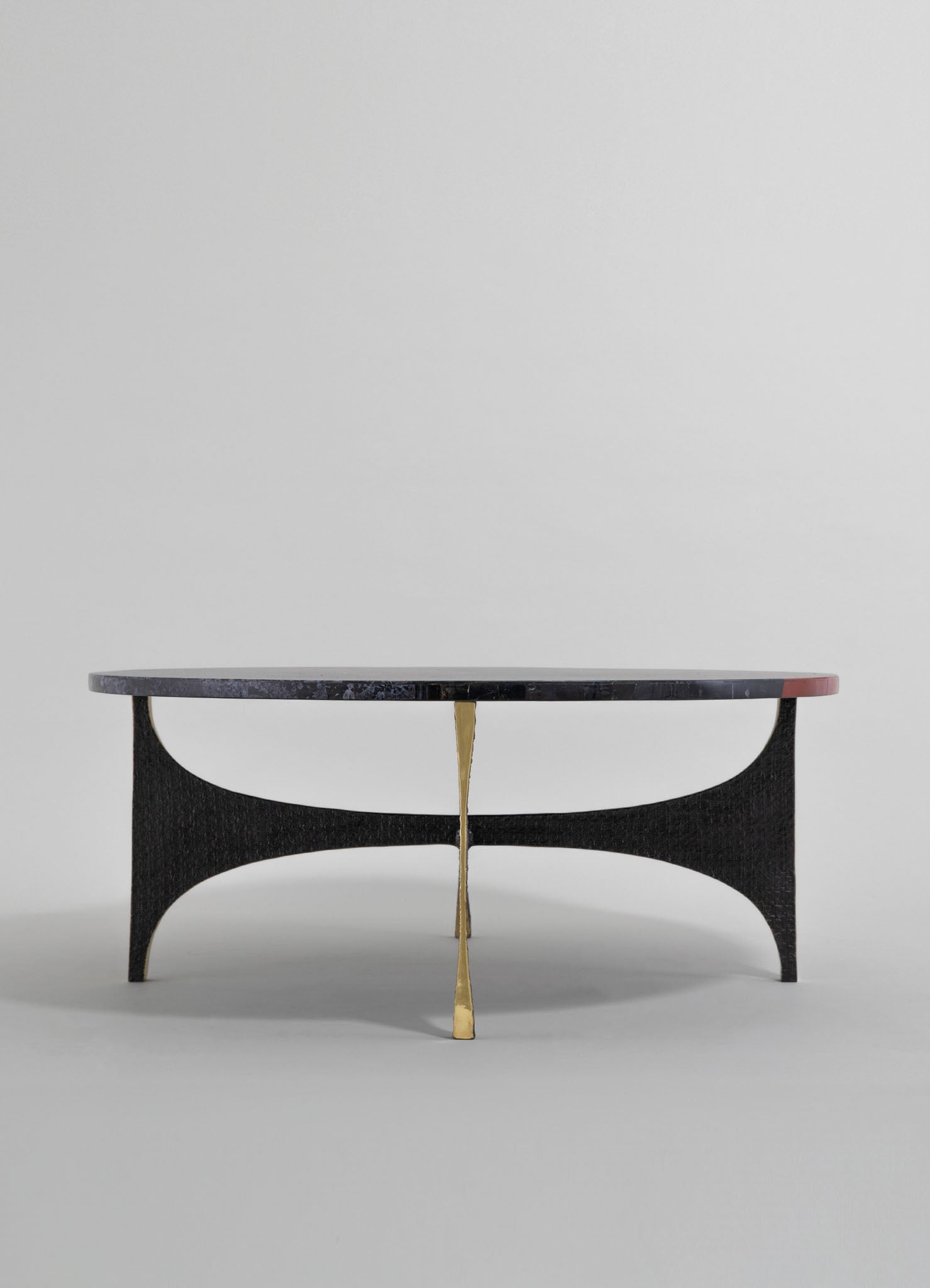 A modern coffee table with a black textured wooden base and a round marble top featuring gray, white, and subtle pink veining, accented with a brass central support.