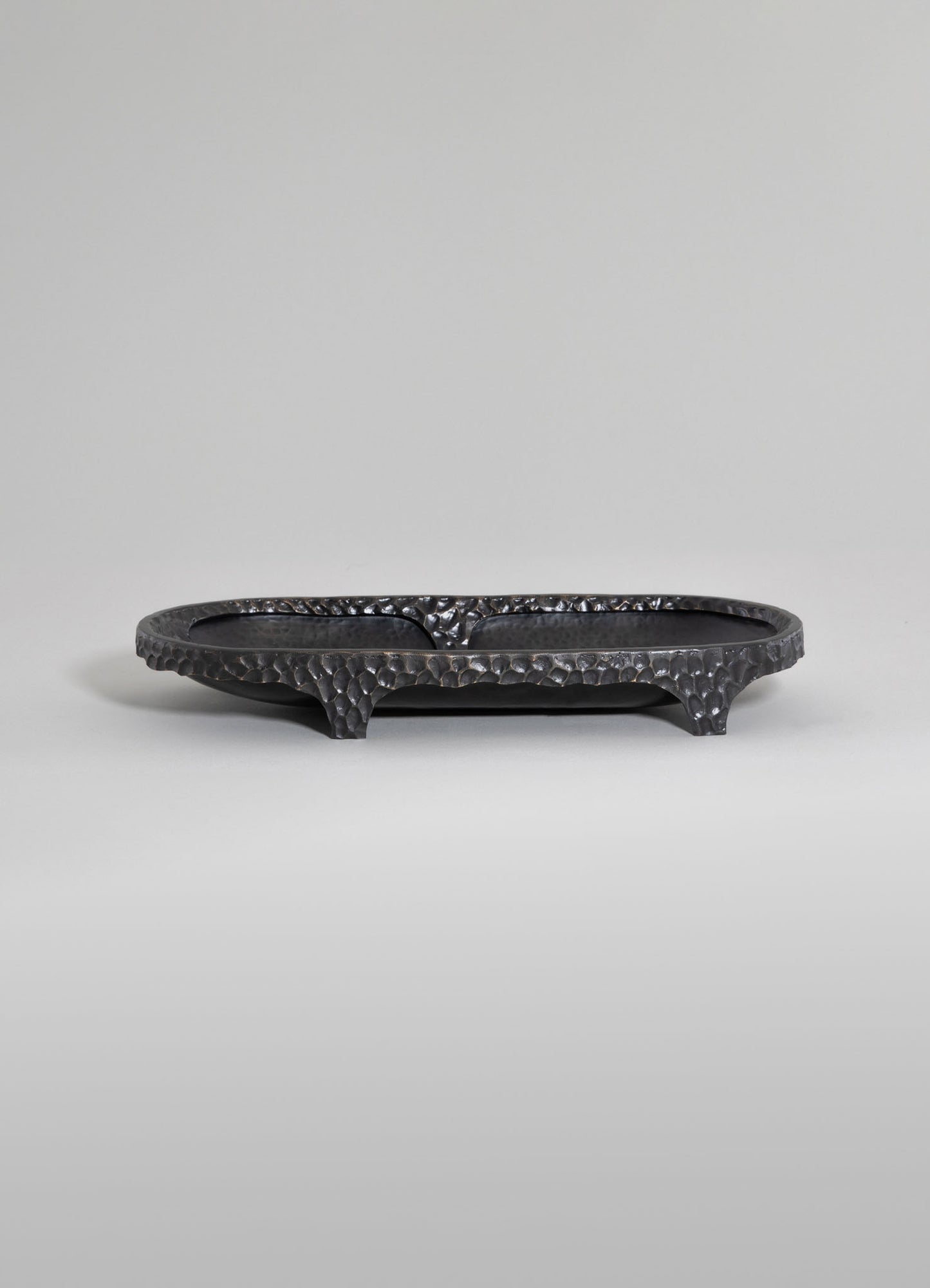 A black hammered metal tray with a textured, irregular surface, raised edges, and curved feet, designed for decorative or serving purposes.