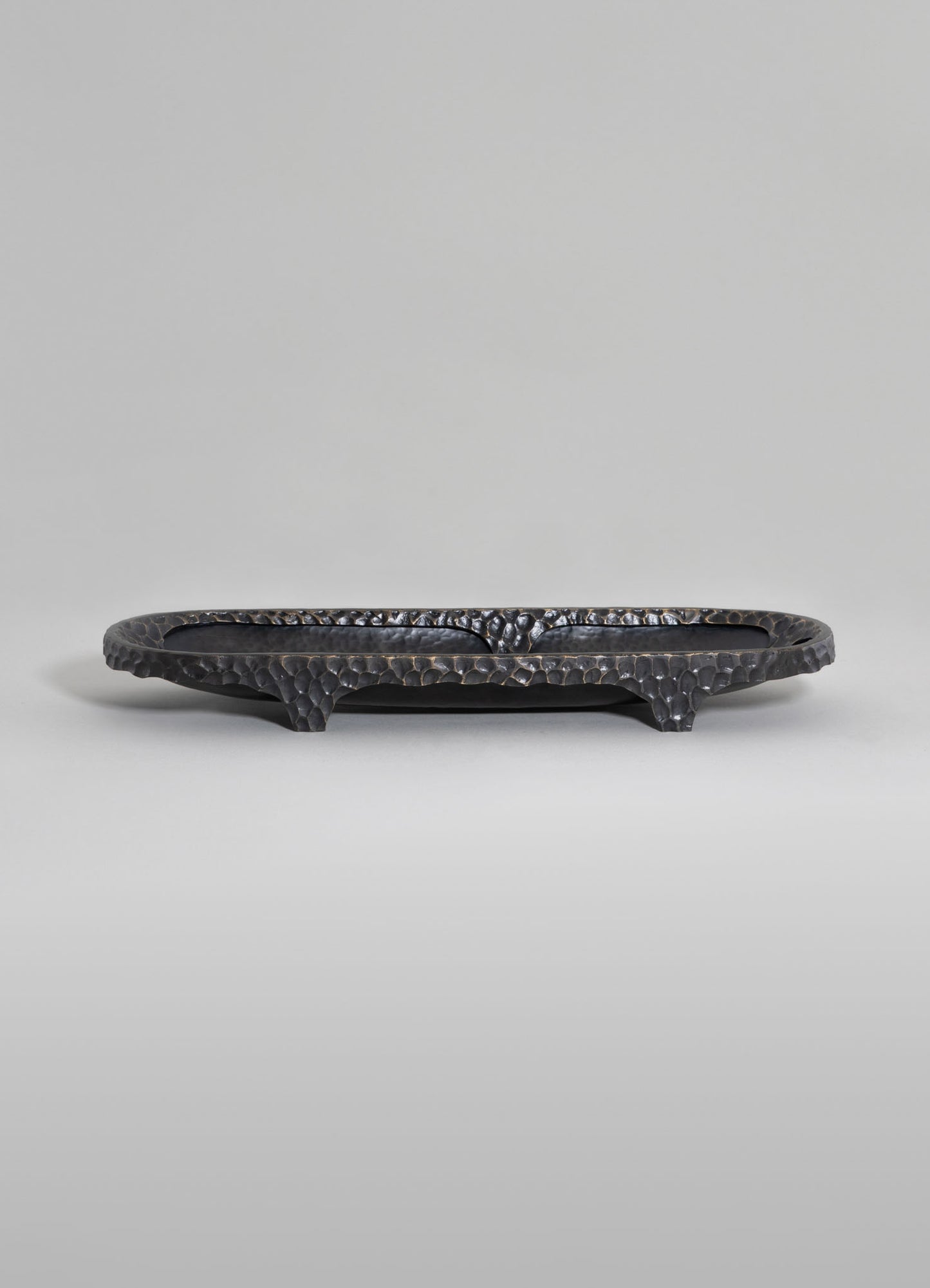 A black hammered metal tray with a textured surface, raised edges, and three ornate legs, exhibiting a handcrafted design.