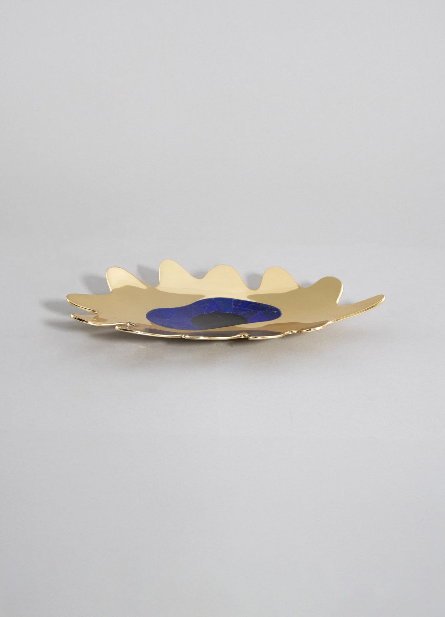 A decorative ceramic plate with a wavy edge, finished in gold with a central design in deep blue and black, presented on a plain light background.