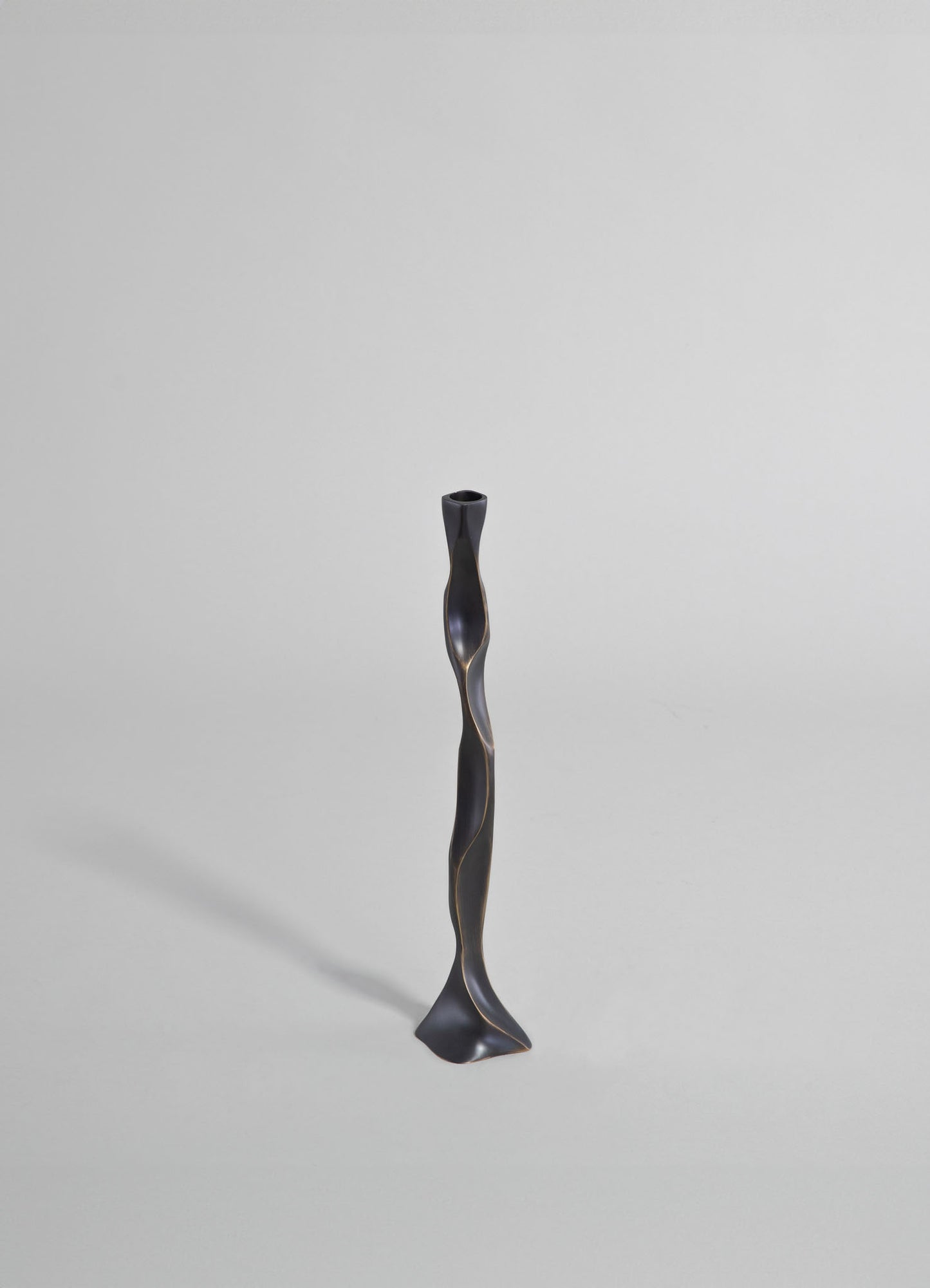 A sculptural candle holder with a twisted, elongated form in matte black finish, featuring subtle metallic accents, standing on a neutral background.