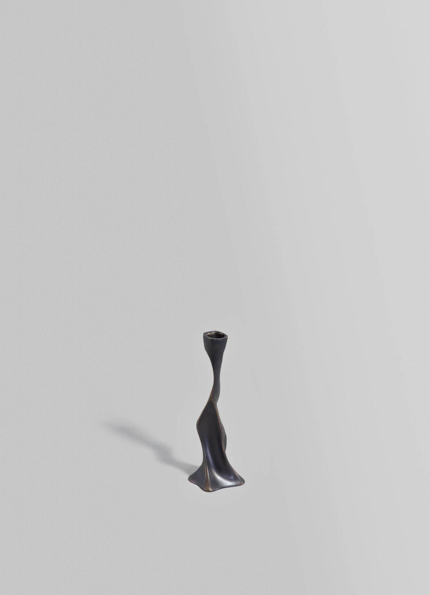 A black metal candlestick holder with a sculptural, twisted design, featuring a wide base and a narrow top for holding a candle.