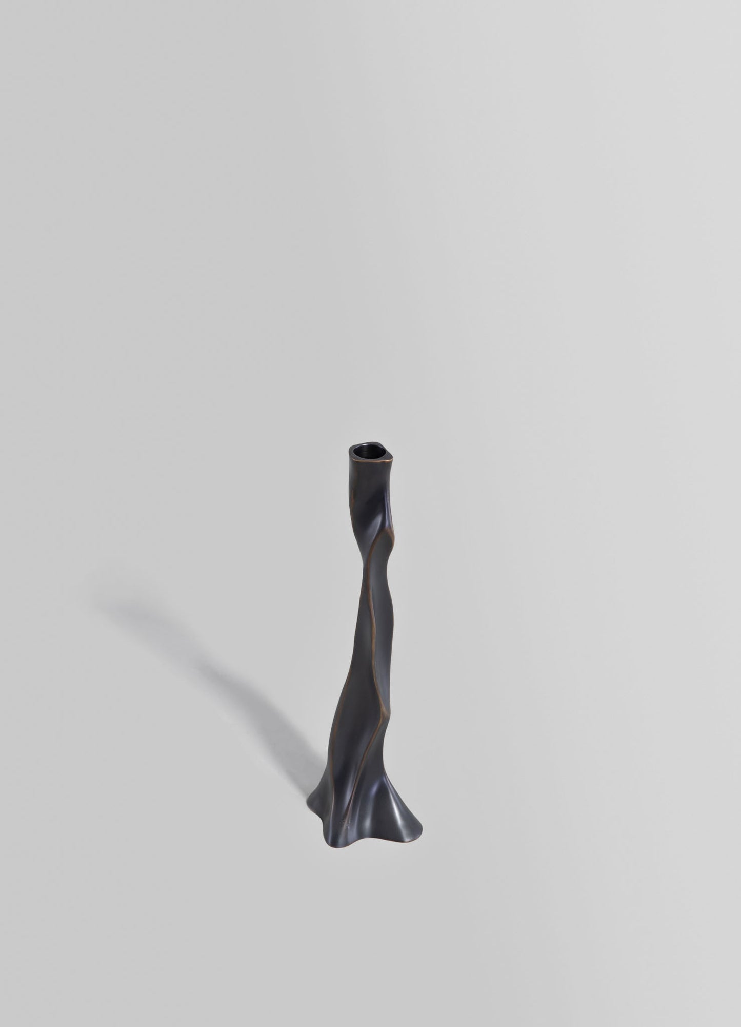 A tall, sculptural candle holder made of dark metal with an irregular, twisted shape and a textured matte finish.