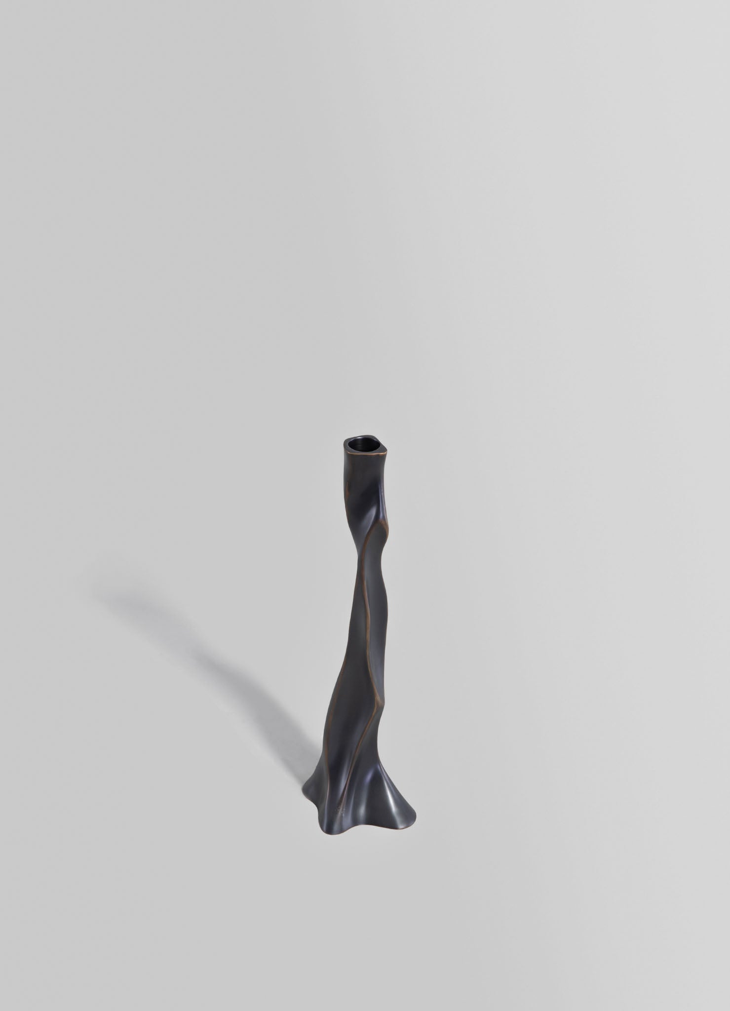 A tall, sculptural candle holder made of dark metal with an irregular, twisted shape and a textured matte finish.
